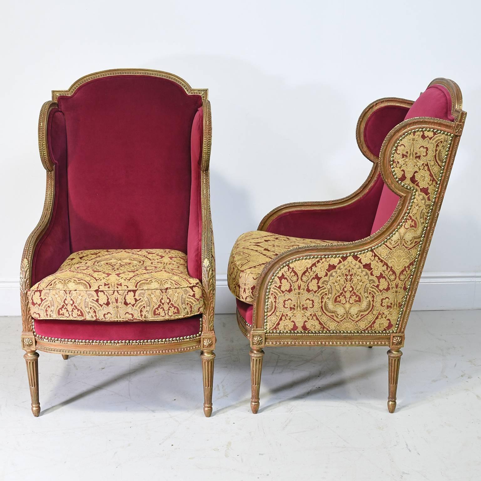 A beautiful and well-proportioned pair of French Louis XVI style bergeres in a light walnut-colored paint over gilded wood with carved acanthus motif, with wingback and resting on turned and fluted legs. Offers upholstered seat back and sides.