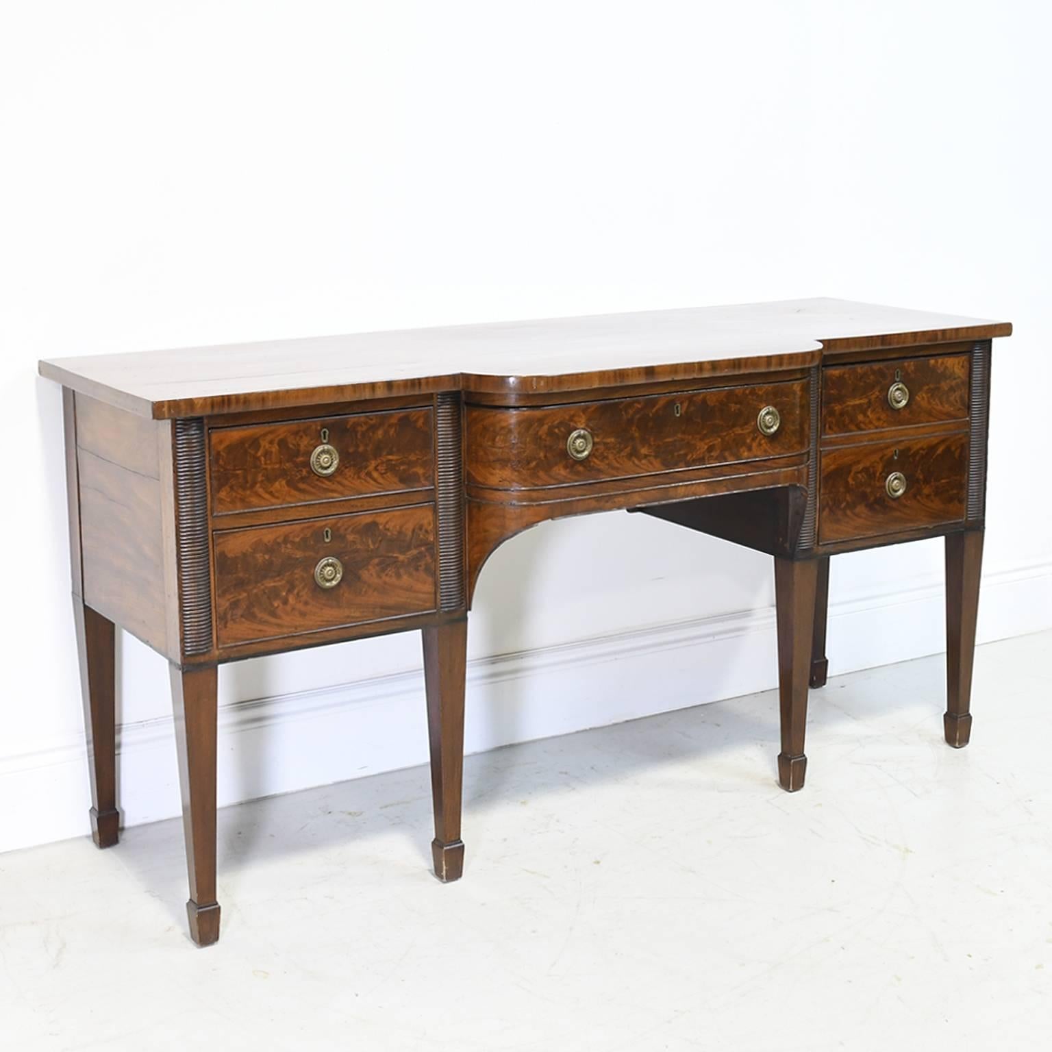 A very handsome English country manor house hunt board / sideboard in figured mahogany from the Georgian period. Features a base that rests on long square tapering legs with spade feet, housing a cellarette drawer for bottles on the right side, two