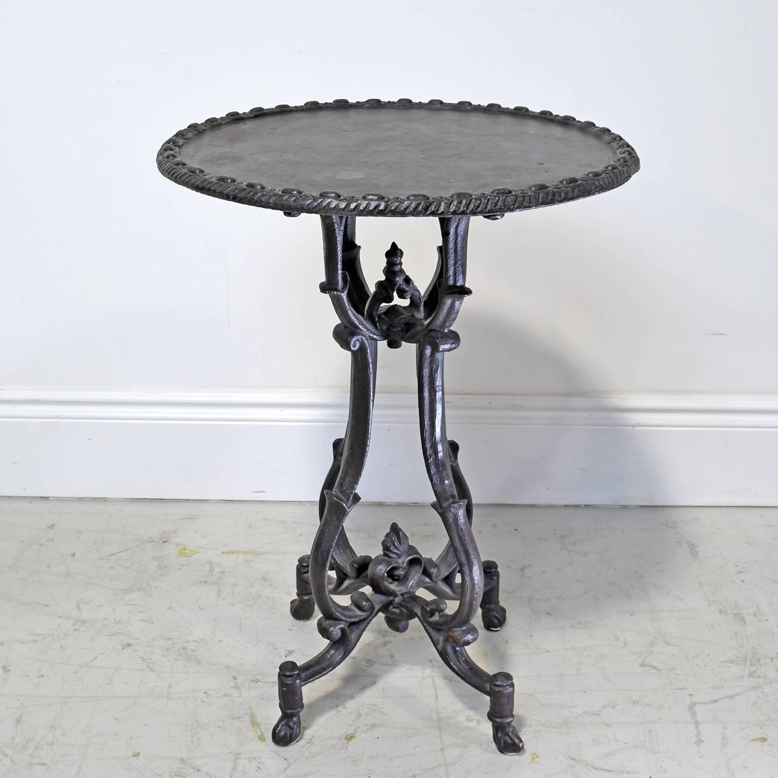 A vintage cast iron garden or bistro table that could also be used as a Stand or end table, with gadrooning along the round top and resting on a cage-shaped base that terminates with four ball-and-claw feet. Color is grey/black gun metal.
