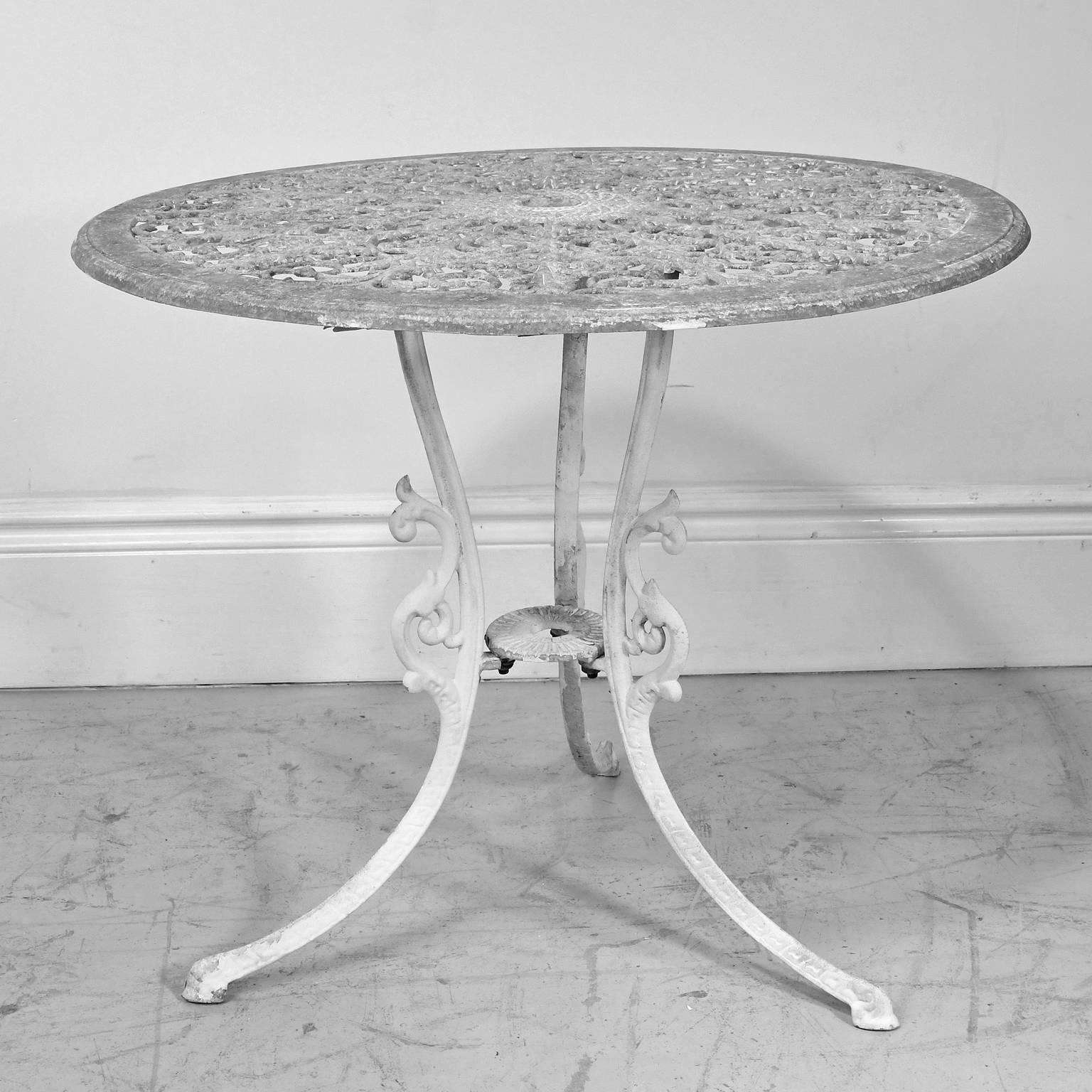 A charming bistro or garden table with round top embellished with a pierced arabesque design and resting on a tripod base with Dutch feet. While offering a sturdy surface for eating, this vintage table is made of light-weight aluminum, making it