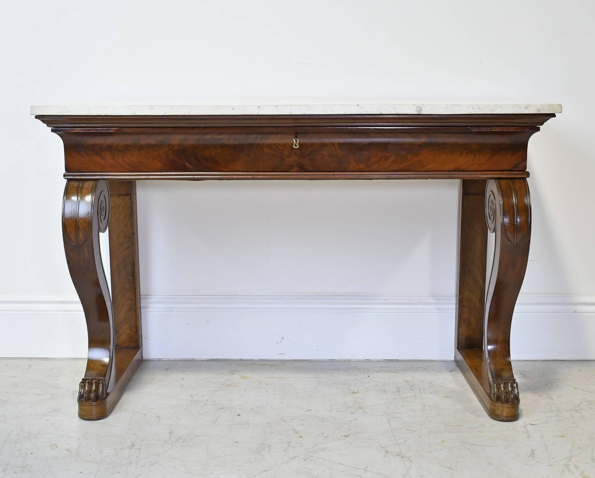 A very handsome French Empire console table in mahogany with white carrara marble top, offering one long storage drawer and resting on a base with 