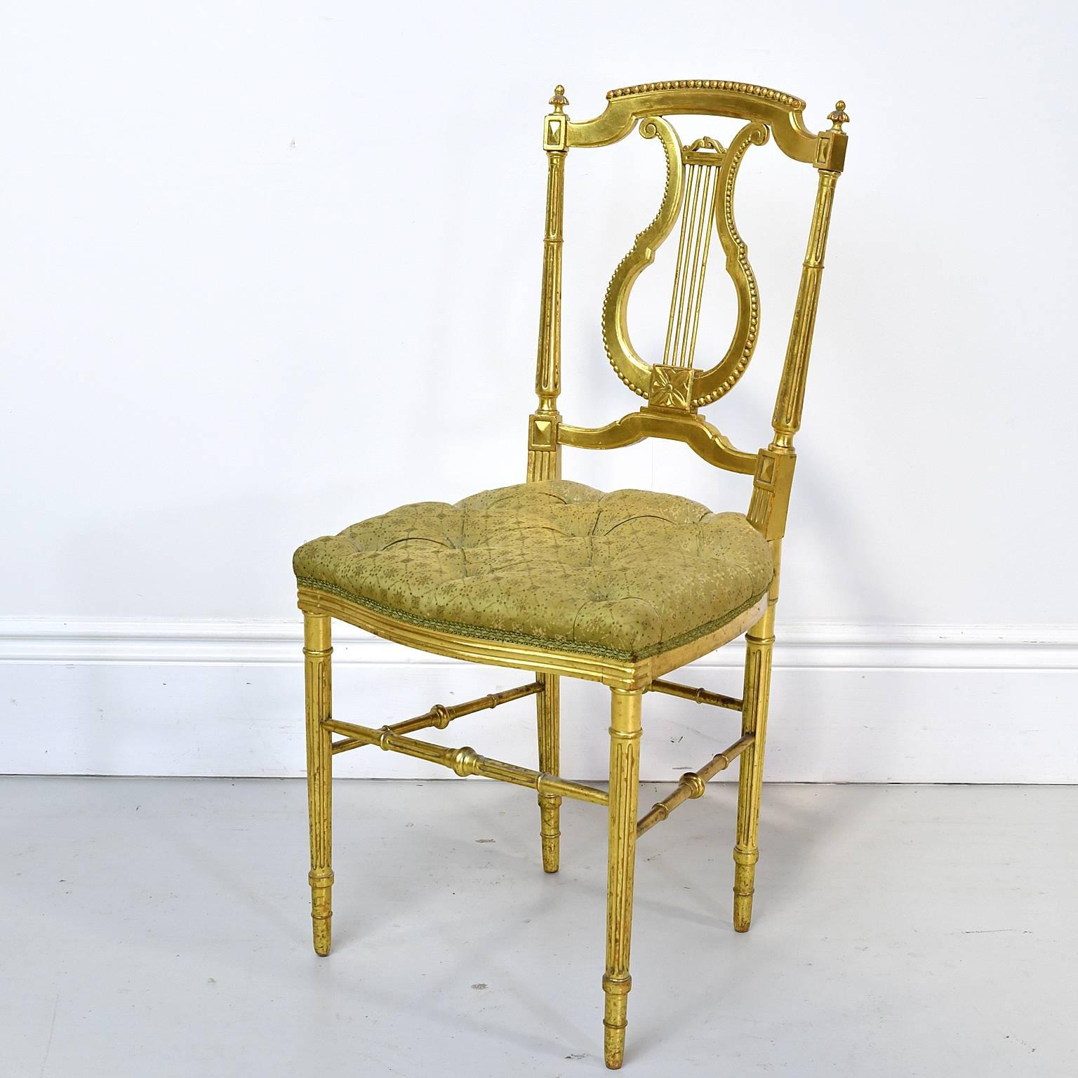 From pre-WWI France, during the Belle Époque period, a very beautiful & fine Louis XVI-style salon chair in giltwood (gold leaf applied over wood) with carved lyre-back, turned and reeded legs with turned box stretcher, and bowed-front seat with