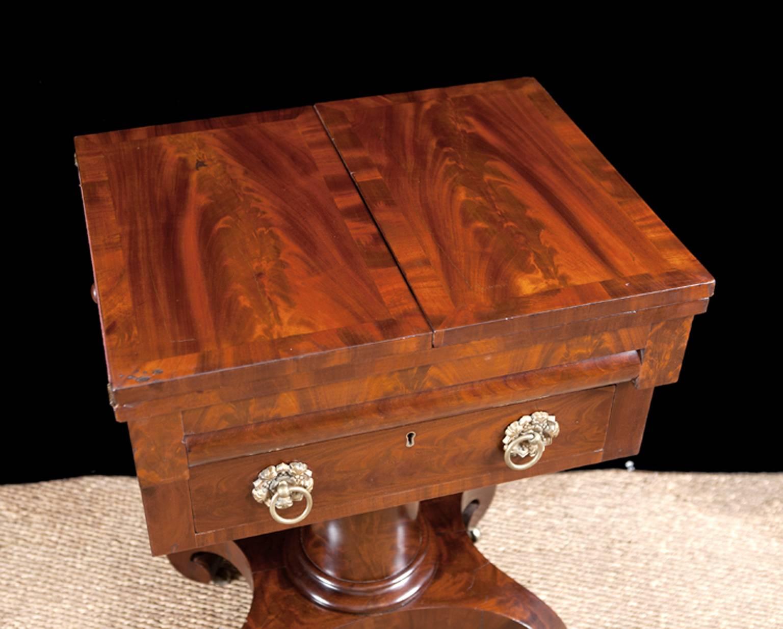 A fine work table in the Grecian Style in mahogany and figured mahogany with two drawers, the first with a convex front. Hinged-top opens to a writing surface with original burgundy baize inset. Cylinder column rests on classical scroll feet.
