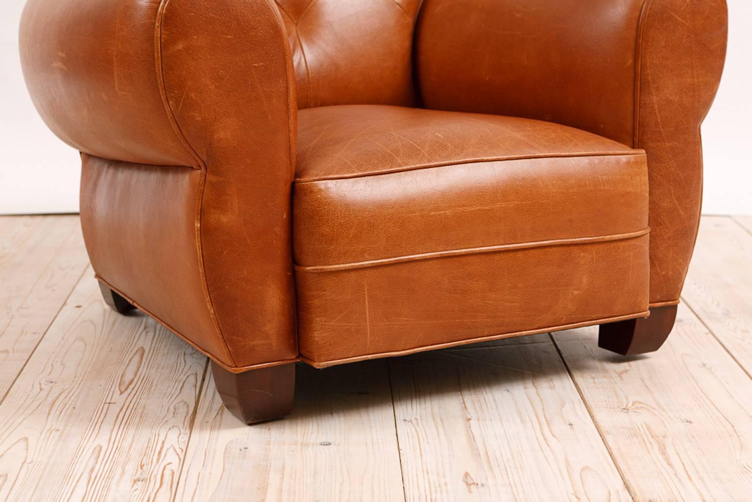 A very comfortable and beautifully-crafted, limited edition, large Art Deco-style club chair upholstered in a caramel-colored buffalo hide with tufted back, rounded arms and wooden club feet. Tight upholstered seat has eight-way-hand-tied spring