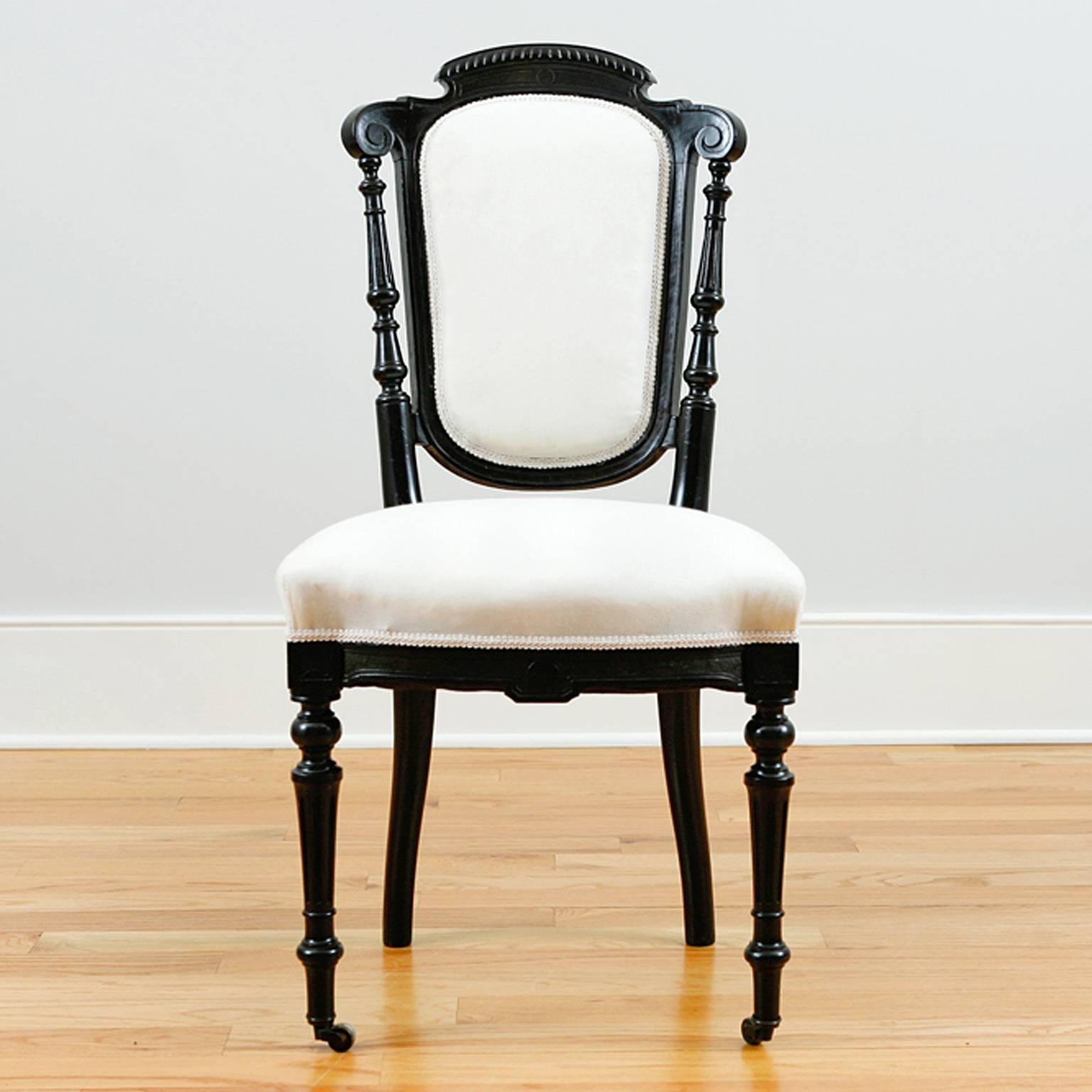 A handsome and very comfortable set of four French dining chairs with upholstered back and seat. Ebonized frame has carved crest and apron, turned front legs with casters and turned back spindles. From the reign of Napoleon III, France, circa