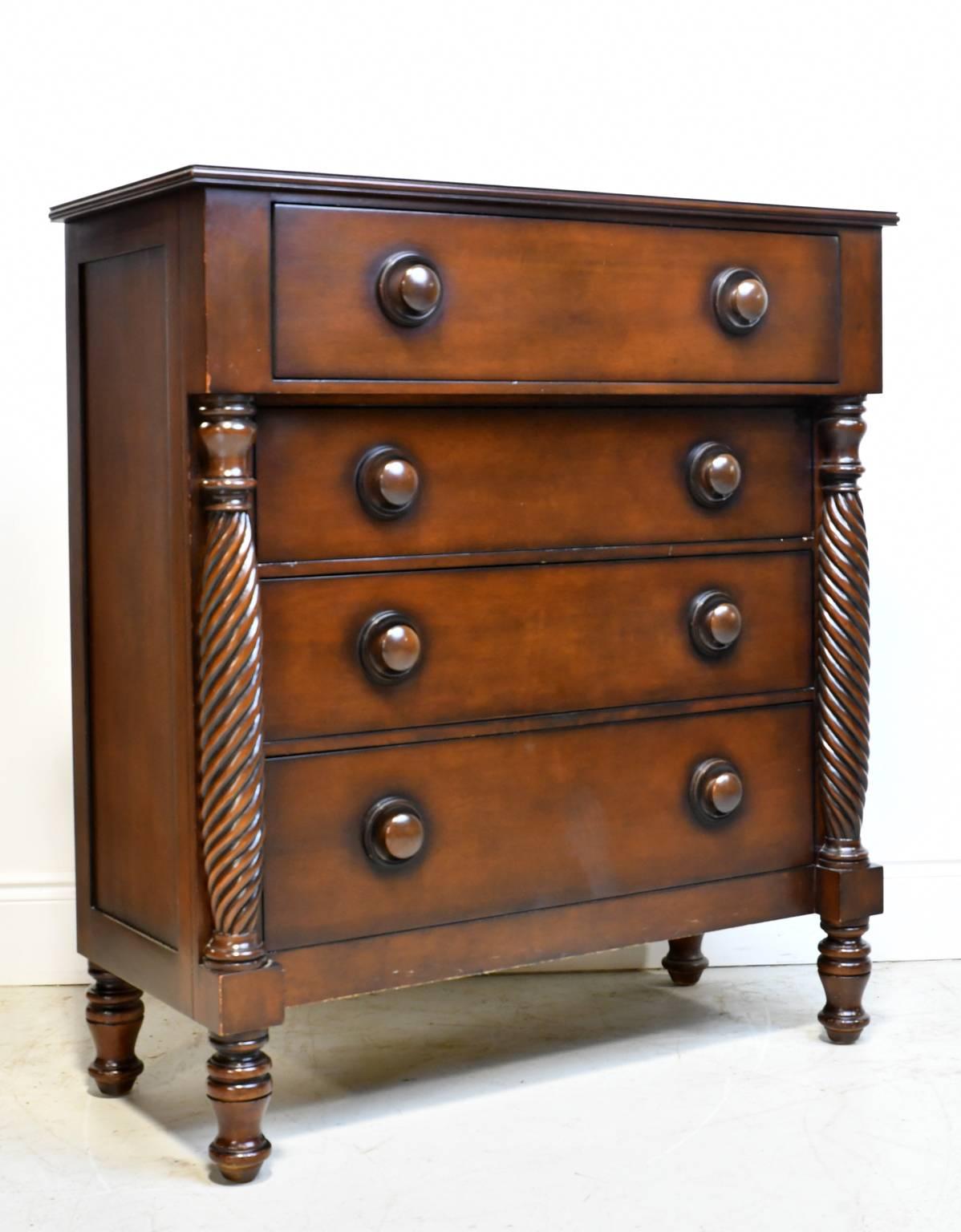 A Ralph Lauren chest in the British Colonial-style in mahogany with four spacious storage drawers that feature inset round wooden pulls. Chest rests on turned feet and features two turned columns with spiral fluting that flank three of the drawers.