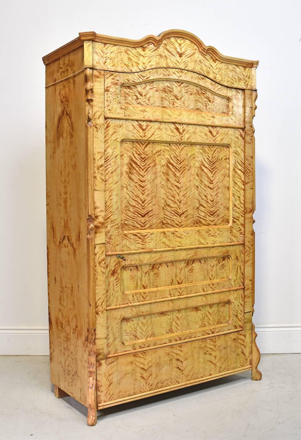 A very beautiful Biedermeier armoire or cabinet in a honey-colored fire birch that has been expertly book-matched throughout to showcase the singular beauty of its grain. The faux front of the single door is paneled to give the illusion of a