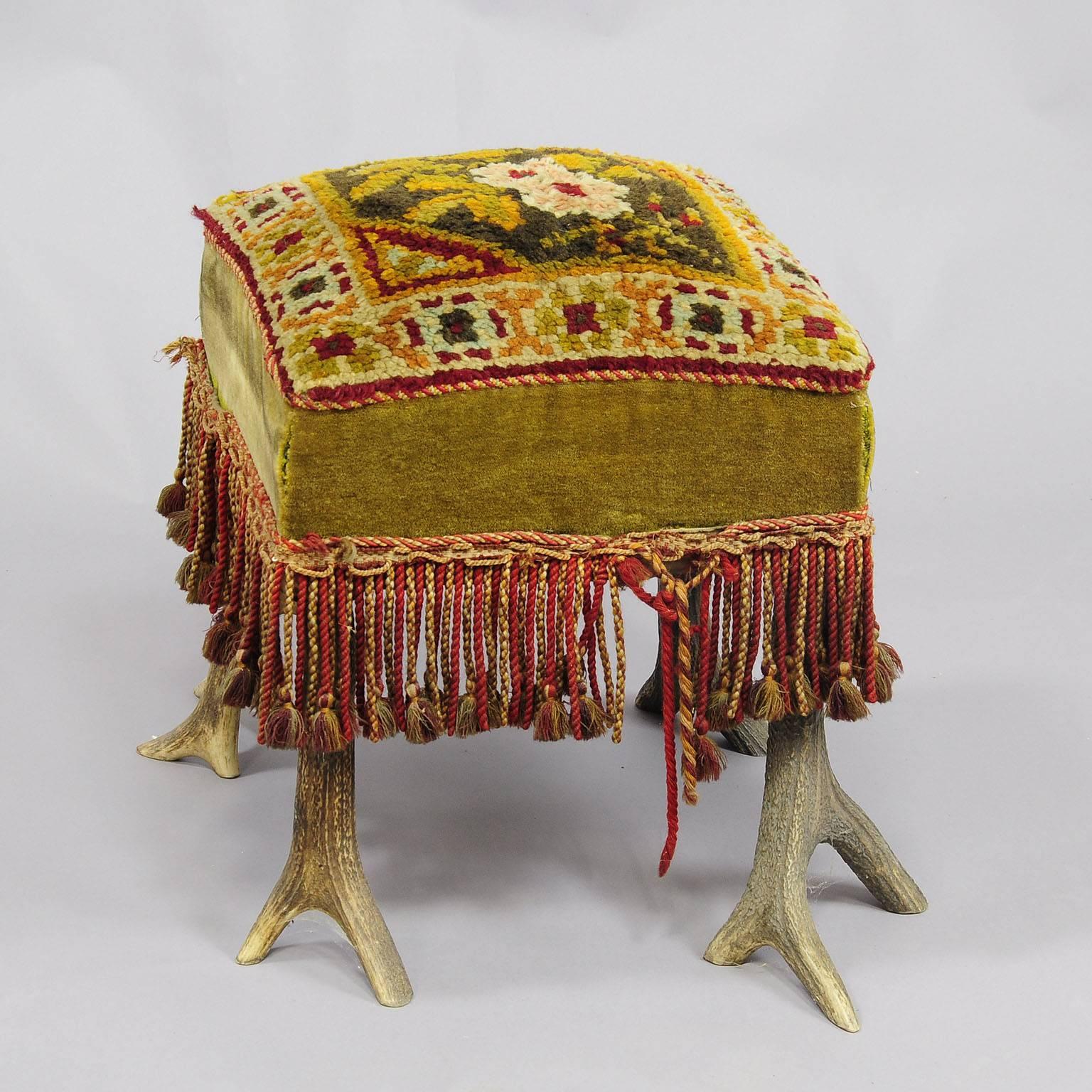 An antique antler stool with stag antlers as legs, upholstered seat with fringes.