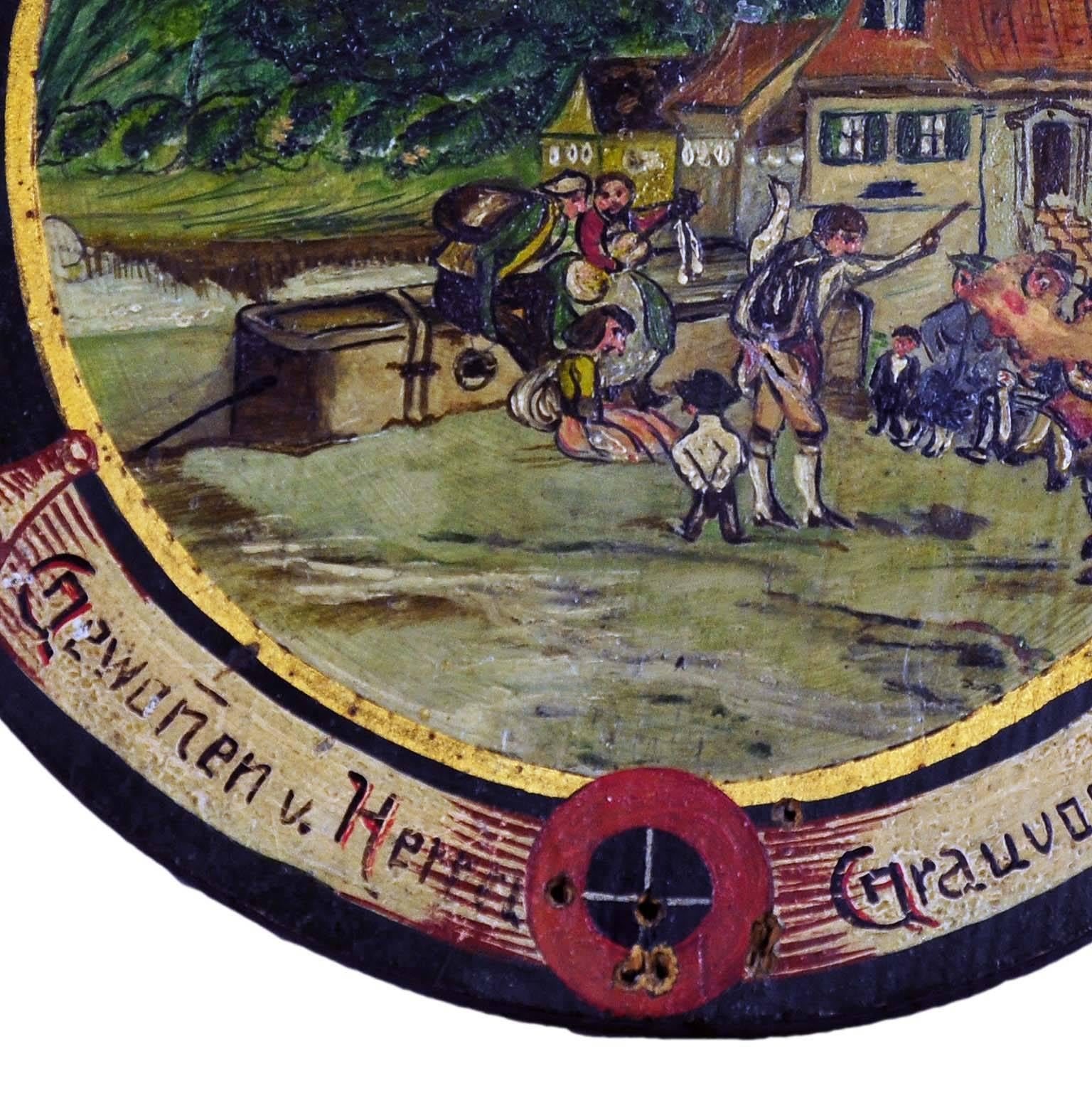 A rare hand-painted antique shooting target depicting a Folksy village live scene. Oil on wood, hand-painted in naive painting style. Bavaria, circa 1920. On the base with impacts of the shooting. On the back handwrite list of the participants of