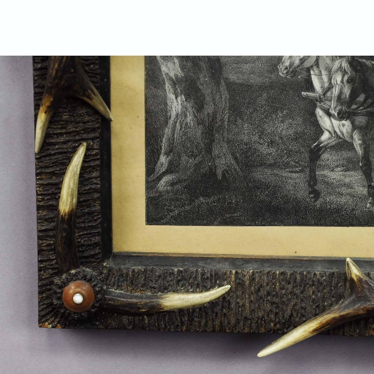 A small antler frame decorated with deer antlers and turned horn roses. Wooden frame covered with stucco imitating antler veneer. Inside an antique copperplate print with scenery in the forest.