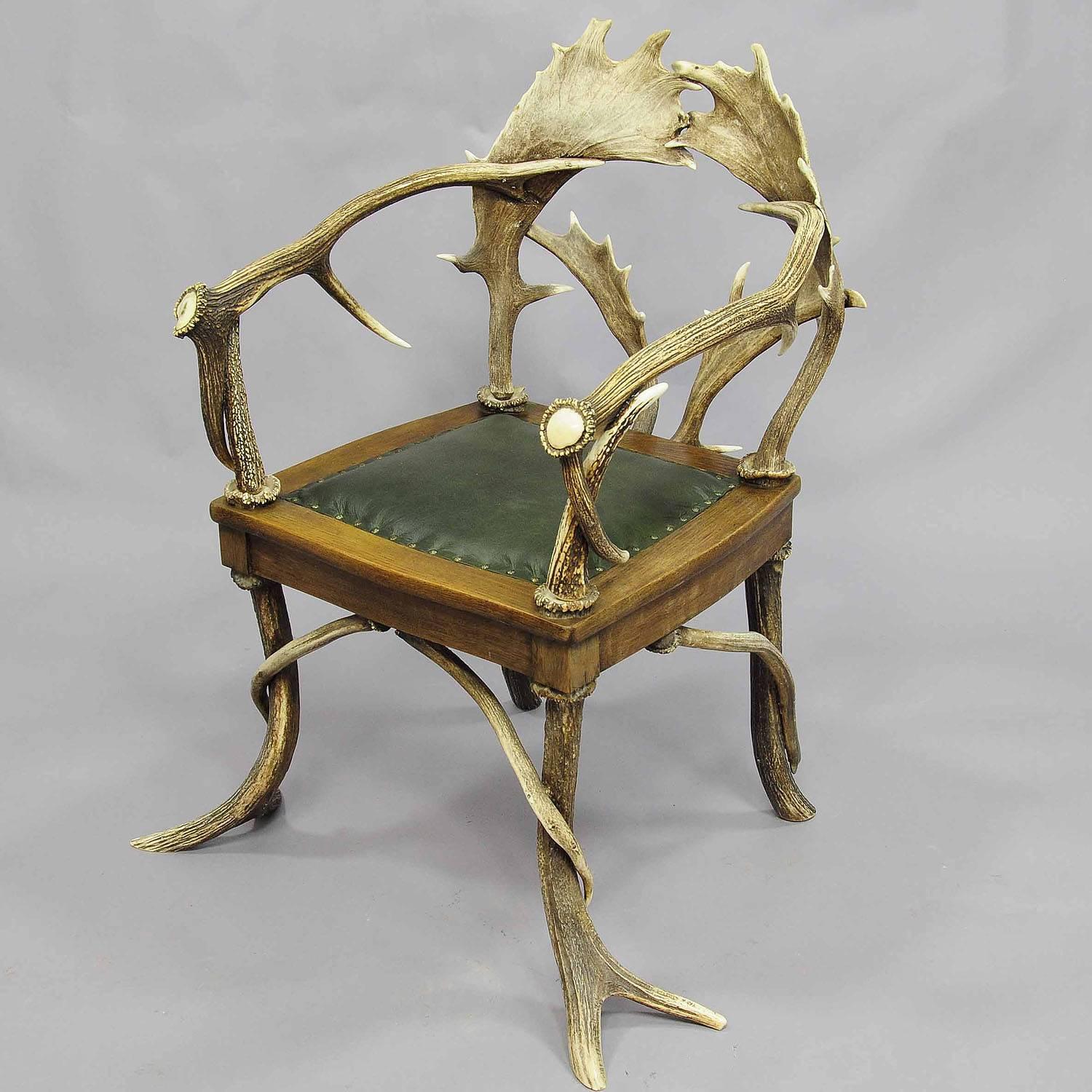 An antique black forest antler armchair, made of horns from the deer and fallow deer. green leather seat (replaced). Executed, circa 1900.