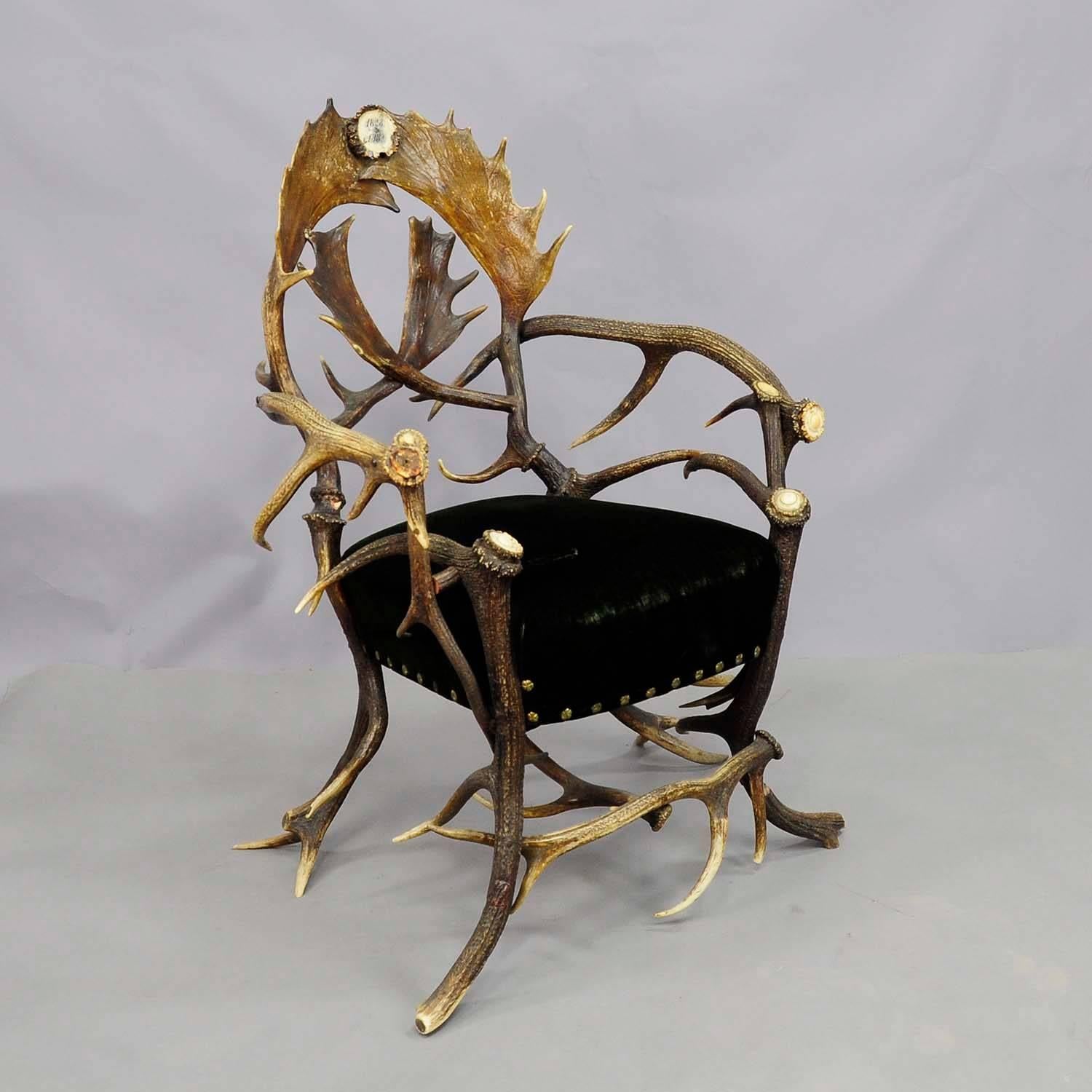 An antique Black Forest antler armchair with real stag antlers as legs and armrests, backrest with fallow deer antlers, upholstered seat with green velvet (needs to be replaced), Black Forest, circa 1890.