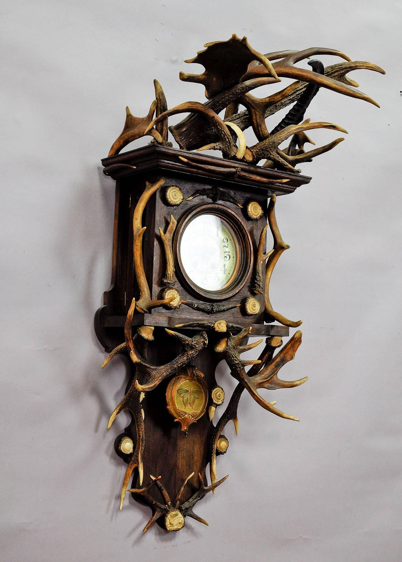 a rare and huge black forest wall clock. oakwood case richly decorated with antlers from the deer and fallow deer, wild boar tusks and carved horn roses. executed ca. 1900. the oak wood case is with glasses on three sides. it has two detailed carved