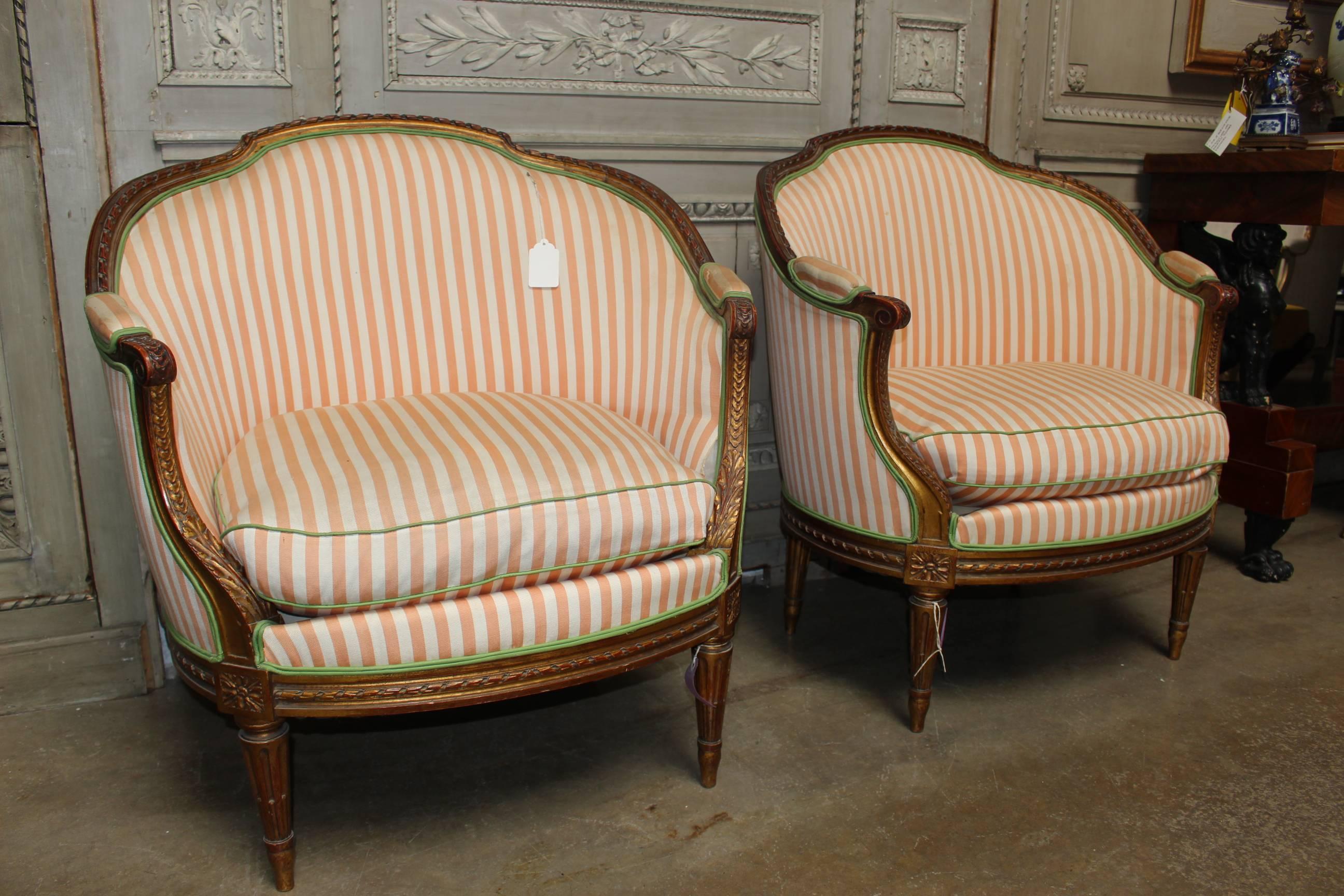 Pair of 19th century French Louis XVI style armchairs. These carved wood chairs are in a gold leaf finish and are known as marquise due to their extra wide seat, typically wider than they are deep, they were originally designed to accommodate wide