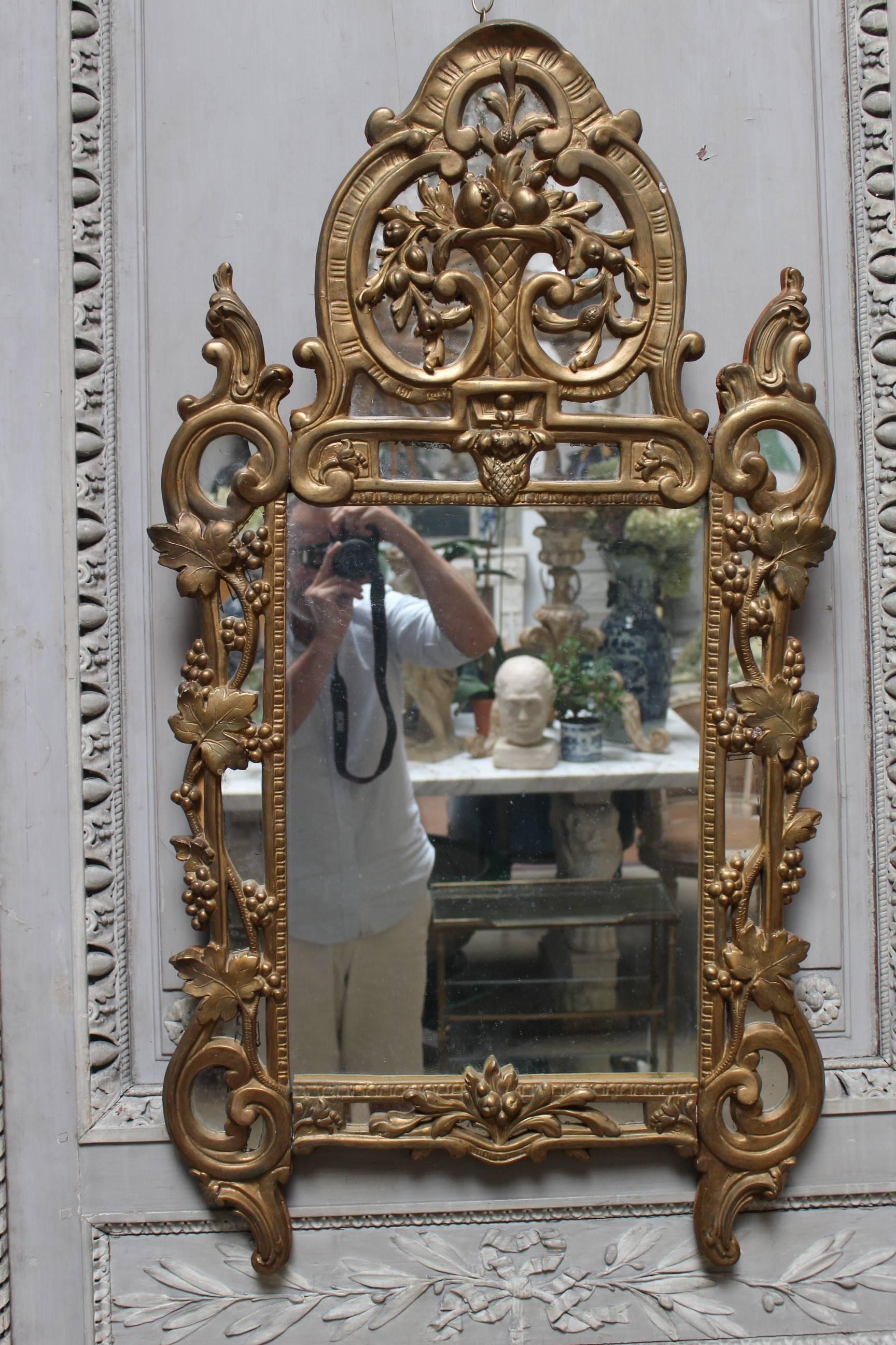 French Regence 18th century mirror with a gold leaf finish. This small mirror is decorated in grapes and vines as well as a conucopia with fruit and flowers. This small period mirror is the perfect scale for a powder room or small space.