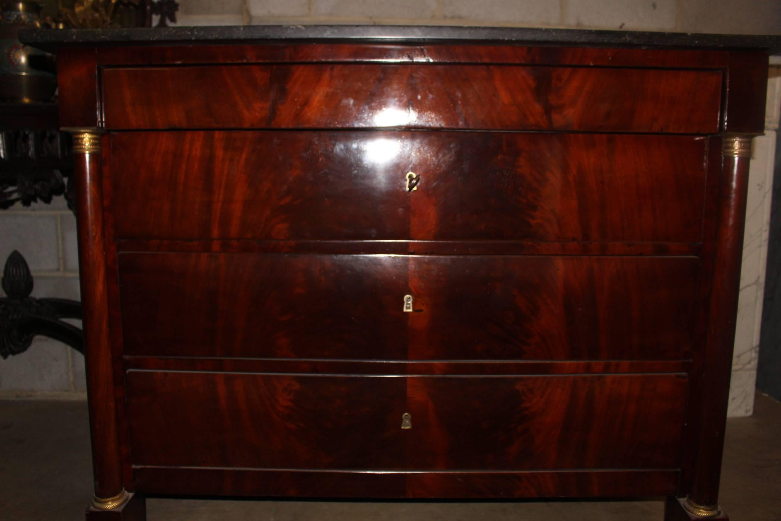 An early 19th century French Empire mahogany commode with bronze mounts and a dark gray stone top.  The chest of drawers is very handsome and functional and is in very good condition. There is a key that opens the drawer leaving the facade very