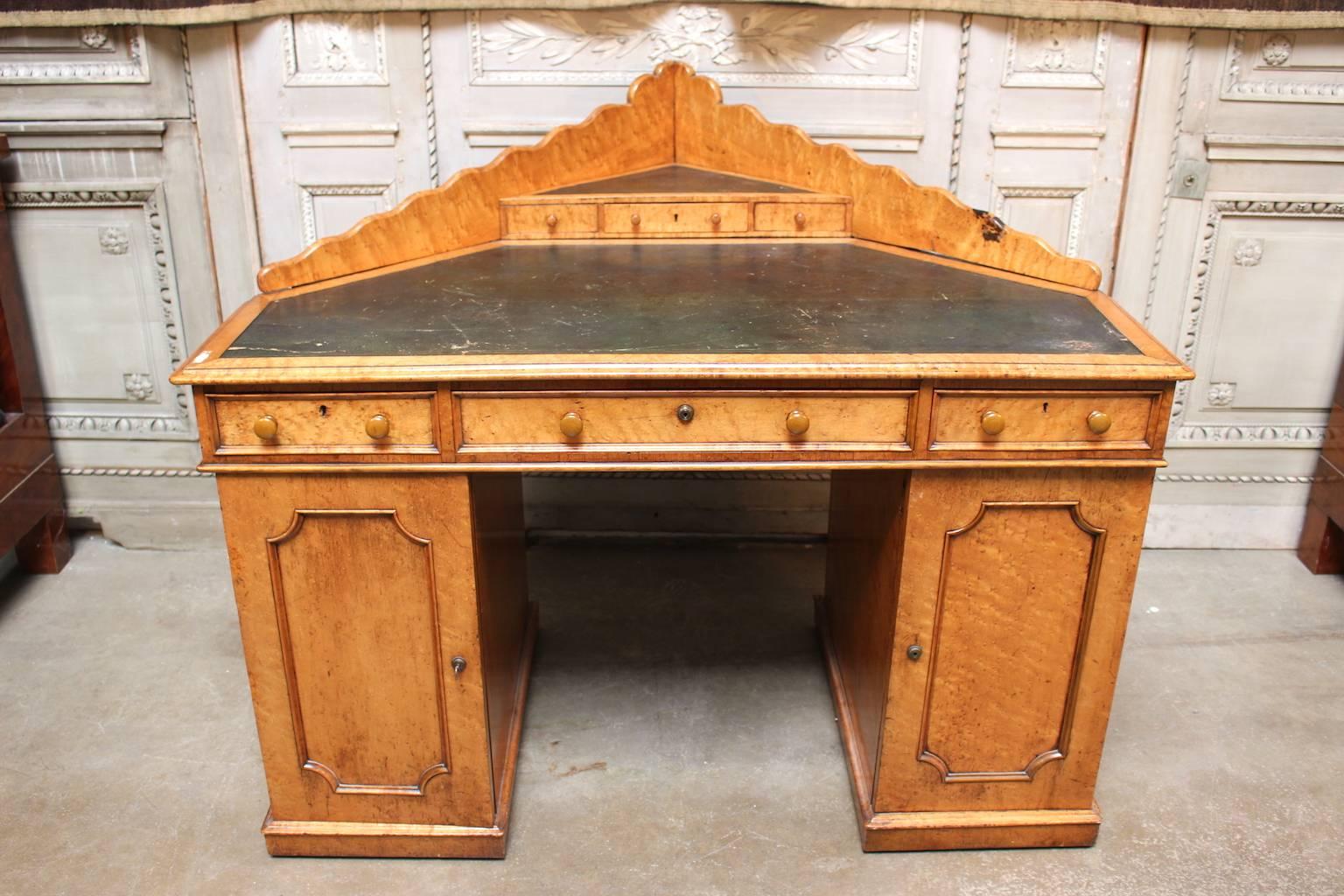 An English Victorian birdseye maple corner desk with an old green leather top with large drawers behind the two front doors with three large and three small drawer. This is a charming piece that is very decorative and unique. This is a period
