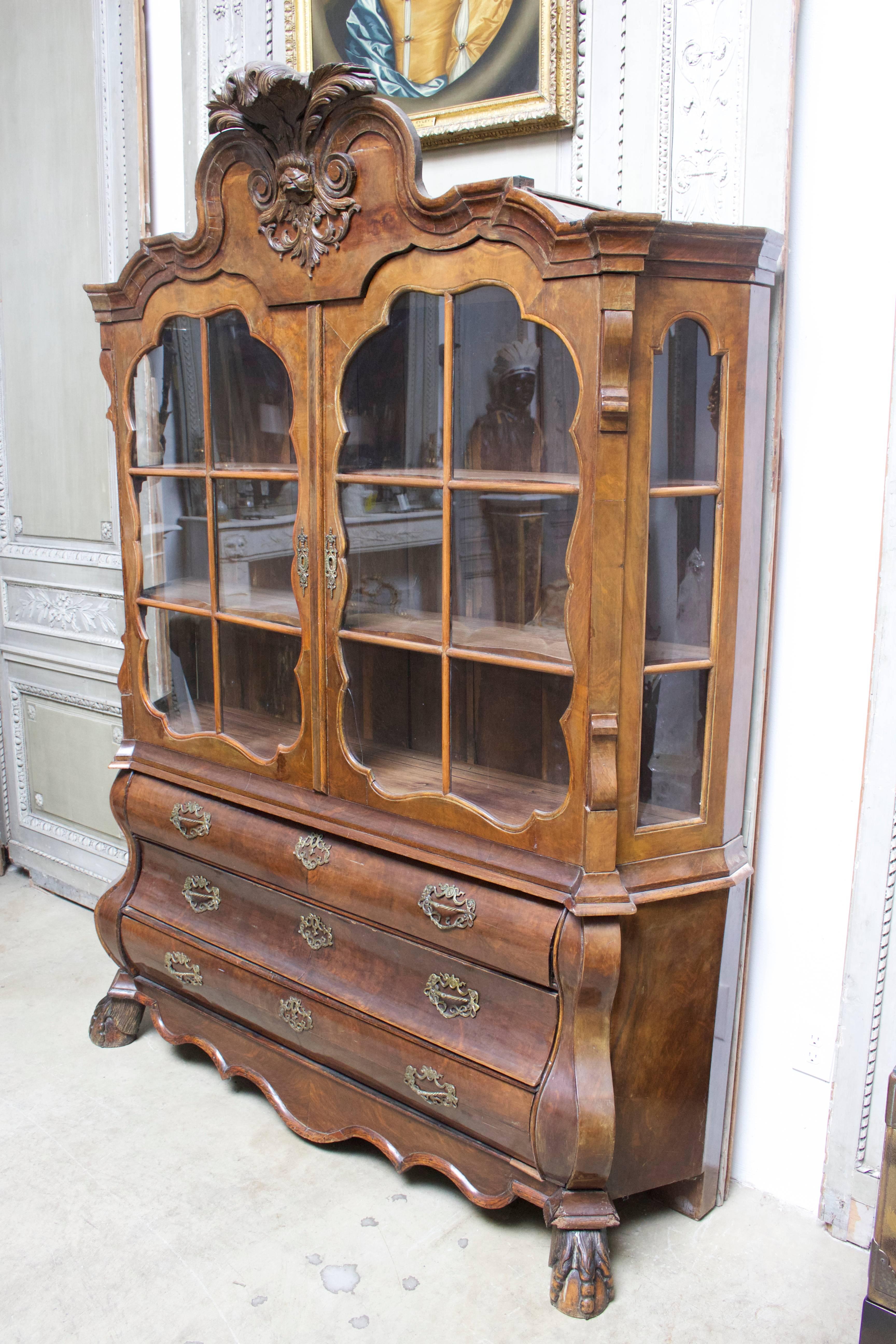 Dutch Rococo style burled walnut cabinet from the 19th century with nice carving and patina. This display cabinet with glass doors and sides rest upon a three drawer bombe chest.