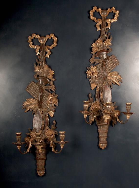 This monumental pair of three-light sconces is hand-carved in mahogany
and gilded with yellow and white gold. The delicate ribbon winds upward
from the candle cups and ties the bundle of wheat sheaves, ending in a
crowning bow. The carvings are
