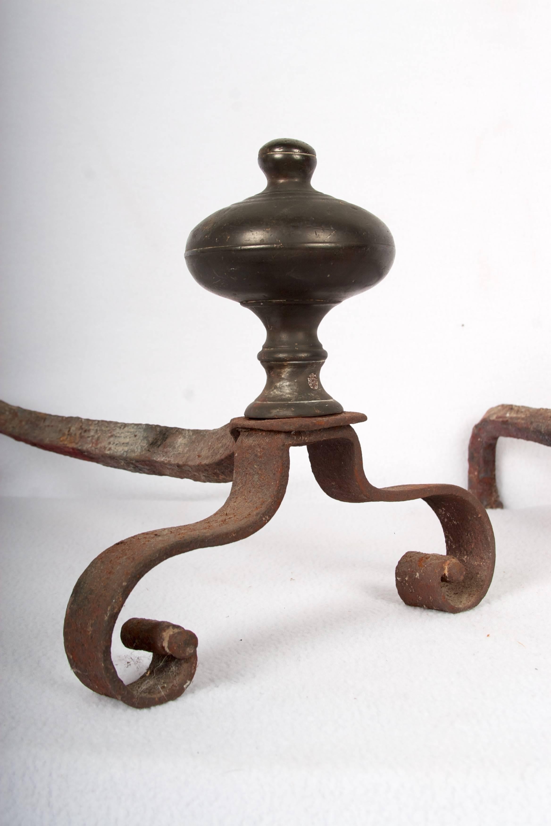 A small rare pair of andirons, hand-forged iron, with patinated turned bronze finial.