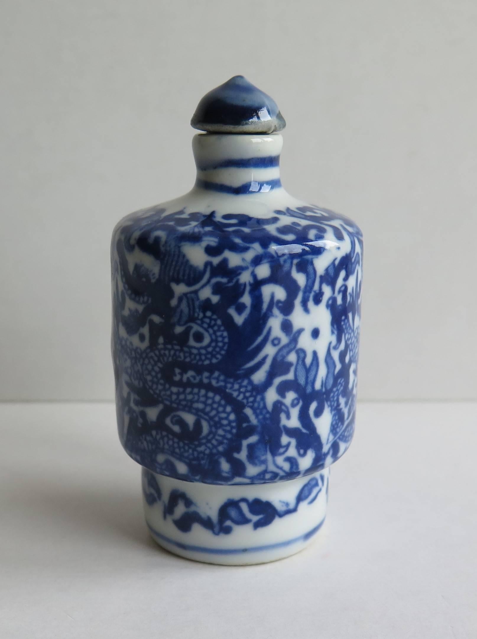 This is a good quality Chinese snuff bottle, made from porcelain, circa 1925.

The cylindrical bottle has a deep foot and narrow neck. The main decoration depicts a well painted continuous dragon design decorated in varying shades of under-glaze