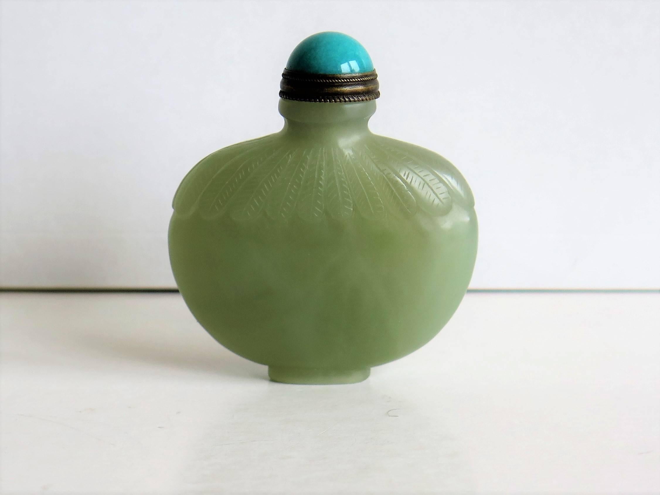 This is a beautiful Chinese jade snuff bottle.

The bottle has a lovely light green celadon color and is hand-carved with lappets on the shoulder.

The stopper has a top of a different material, possibly stone and of a slightly mottled aquamarine