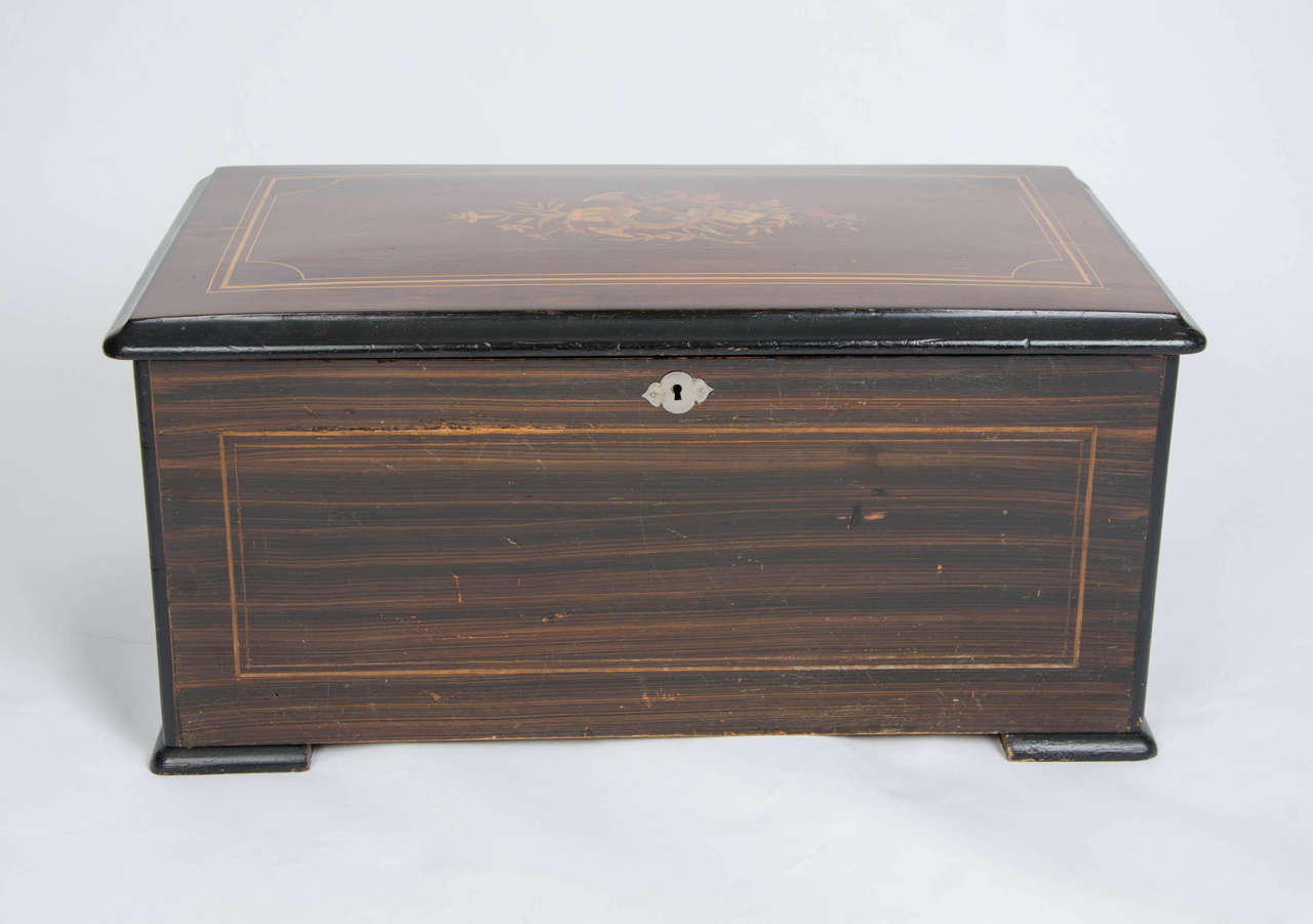 This is a fine quality Swiss 10 Air Music box, dating to circa 1880. 

The mechanical mechanism is housed in a rosewood box which has various good inlays. To the top is a marquetry musical scene with inlays of boxwood, maple, fruitwood and other