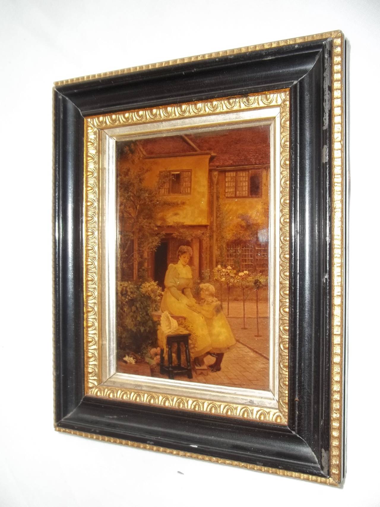 This is a good late Victorian Crystoleum picture, circa 1890.

The picture shows a woman and girl (mother and daughter) in the pathway of an old house. The glass is concave. The frame is of the same period, probably original, with some slight wear