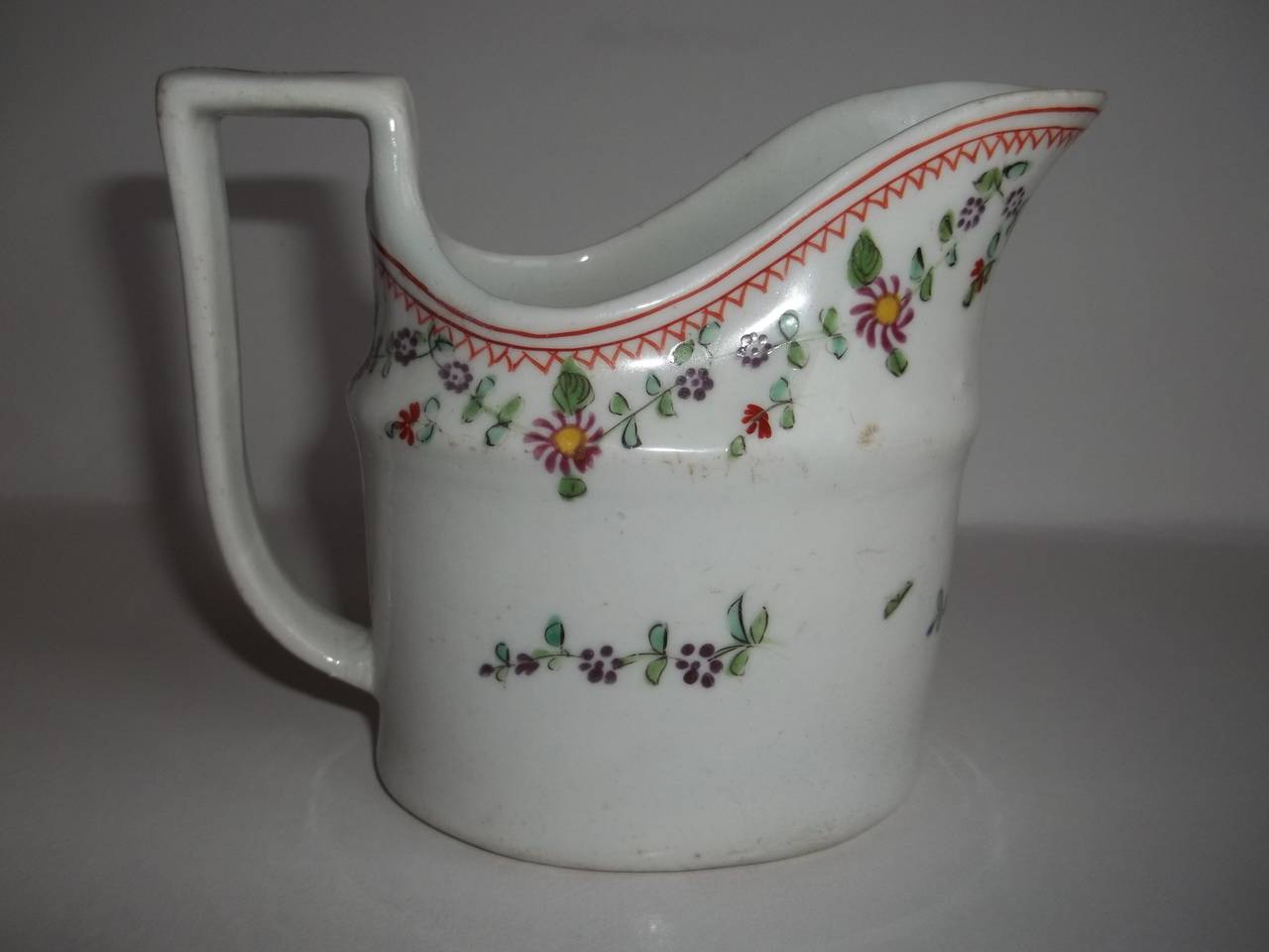 This is an elegant, hard paste porcelain, silver shaped milk jug or creamer made by the John Rose Coalport factory, England circa 1800. 

It has an oval shape with a high loop handle. 

The creamer is beautifully hand decorated with a simple floral