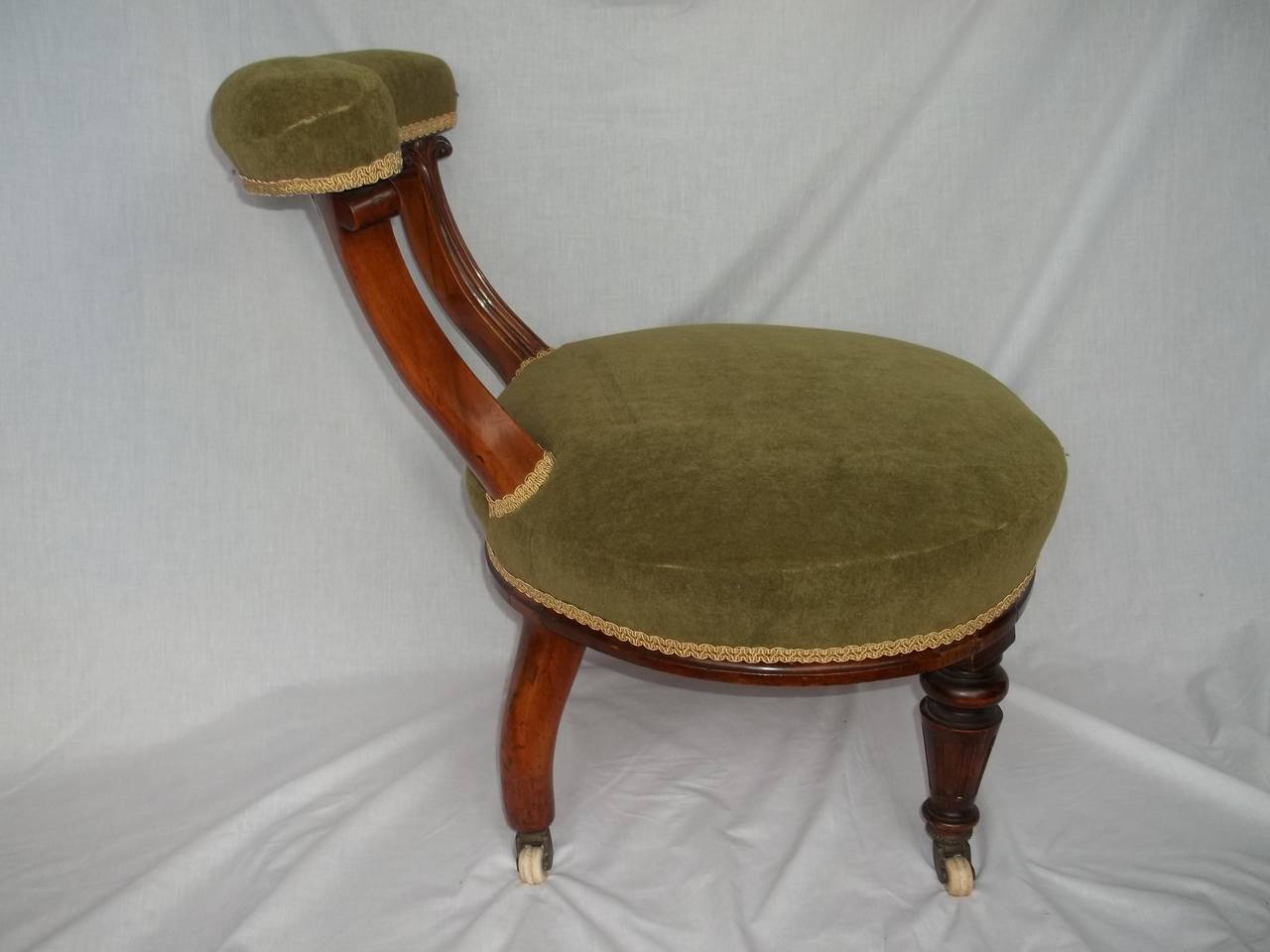 This is a very attractive English nursing or occasional chair from the William IVth period of the early 19th century, circa 1830.

The frame is made of walnut and the oval seat is upholstered in a green velvety fabric, edged with an antique gold