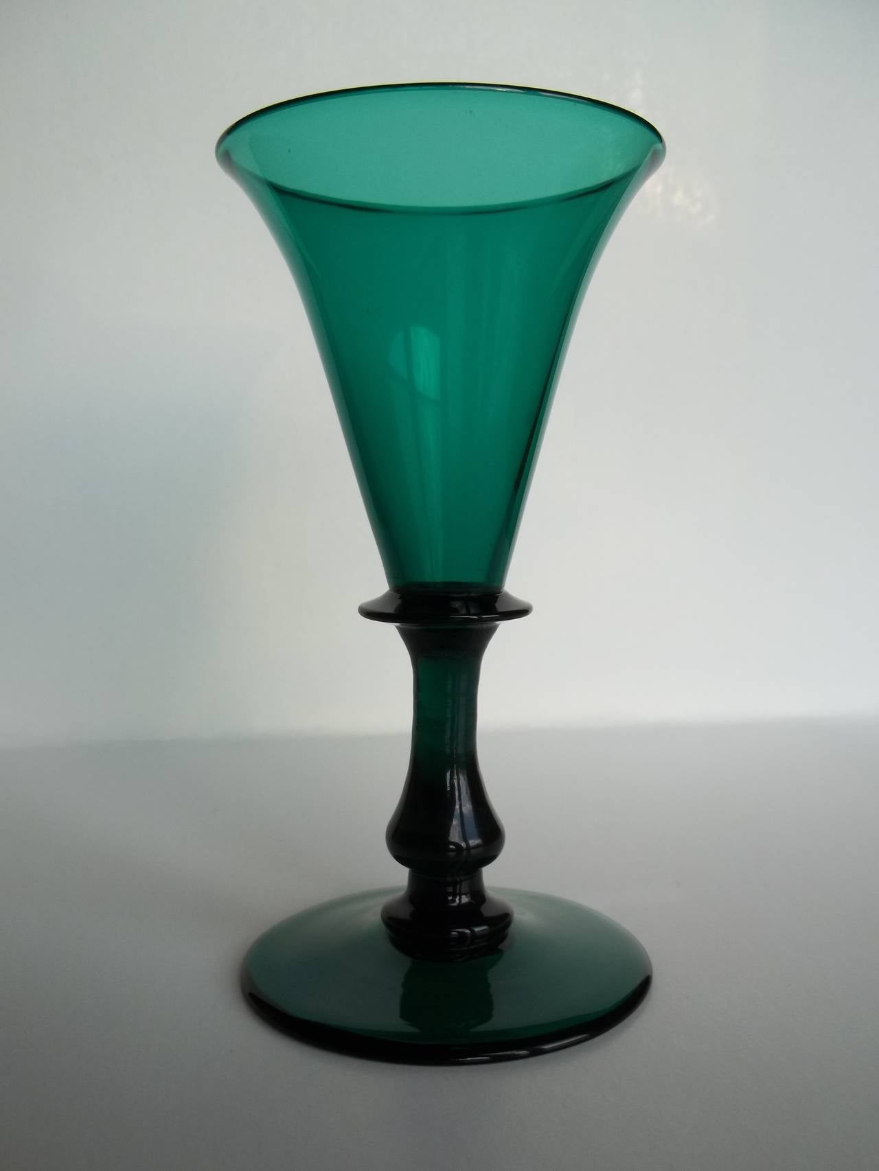 Se trata de un excelente ejemplo de copa de vino verde de Bristol, soplada a mano, inglesa, de principios del siglo XIX, que fechamos en el periodo de Regencia de Jorge 111, hacia 1815.

Este vaso tiene un elegante cuenco en forma de campana con