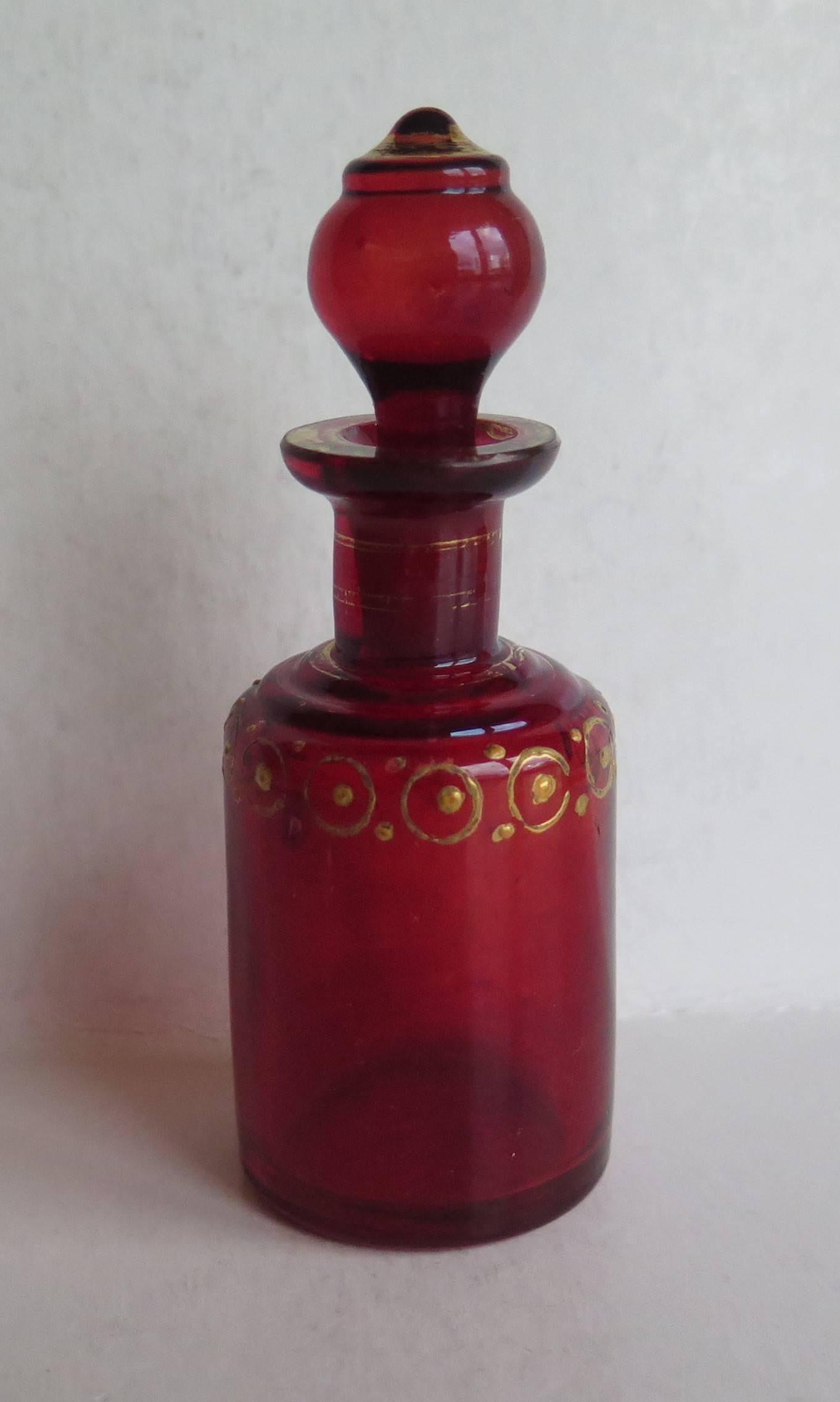 This is a good quality and very attractive Victorian glass perfume bottle, Ca 1870.

The circular bottle is made of moulded ruby glass and has its original stopper. 

The bottle has been hand decorated in gold around the top below the neck with a