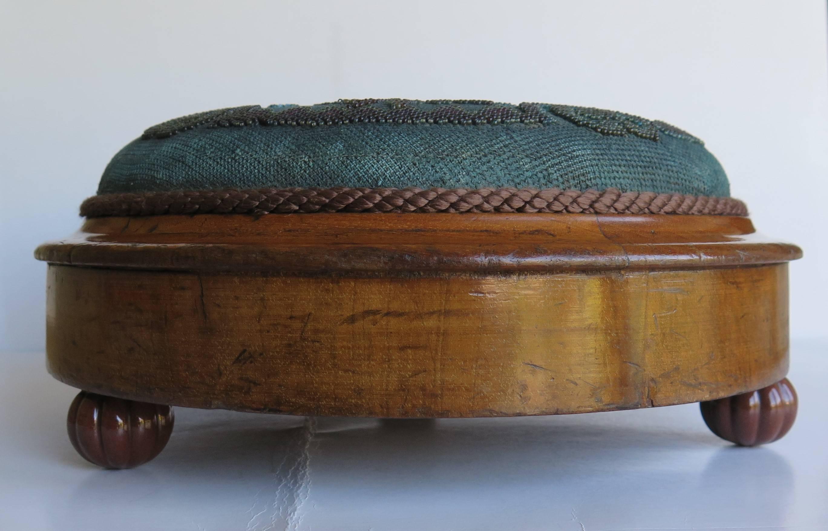 This is a very good example of a beaded English foot stool dating to the mid-19th century of the Victorian period.

The stool is circular with a shaped walnut frame sitting on three fluted ceramic bun feet. The top is upholstered in a teal blue /