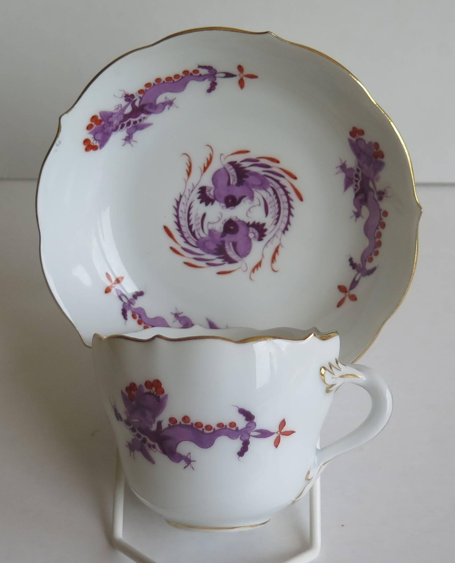 This is a small demitasse cup and saucer by the Meissen factory in fine white porcelain.

The cup and saucer both have wavy edges and the cup has a twisted branch handle with leaf attachments. They are beautifully decorated in a multi shaded purple