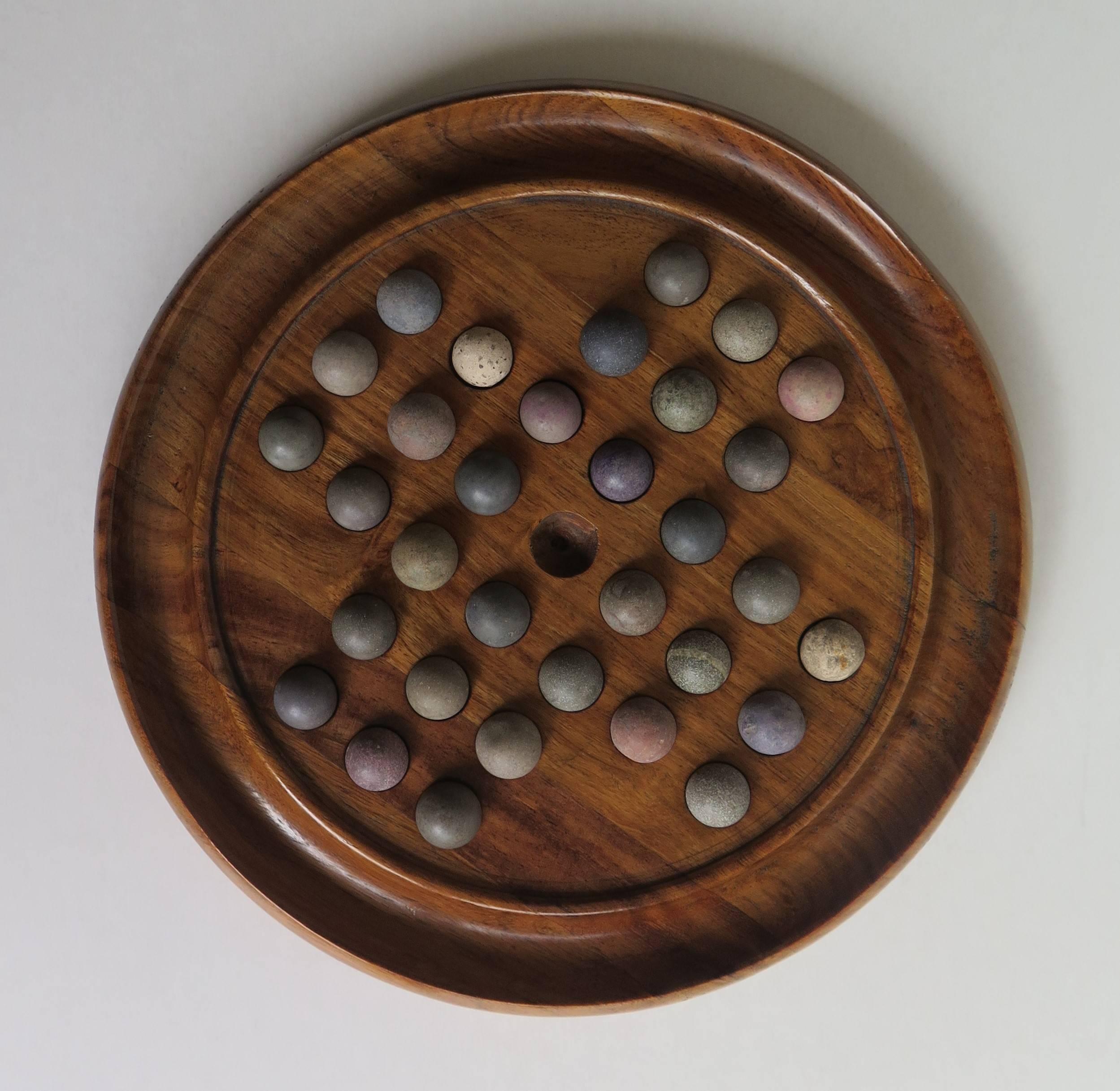 This is a small game of marble solitaire, having a very good board and a complete set of early marbles. 

The circular turned board is made of walnut and has an excellent grain and color. The board has 32 equi-spaced holes with an additional one
