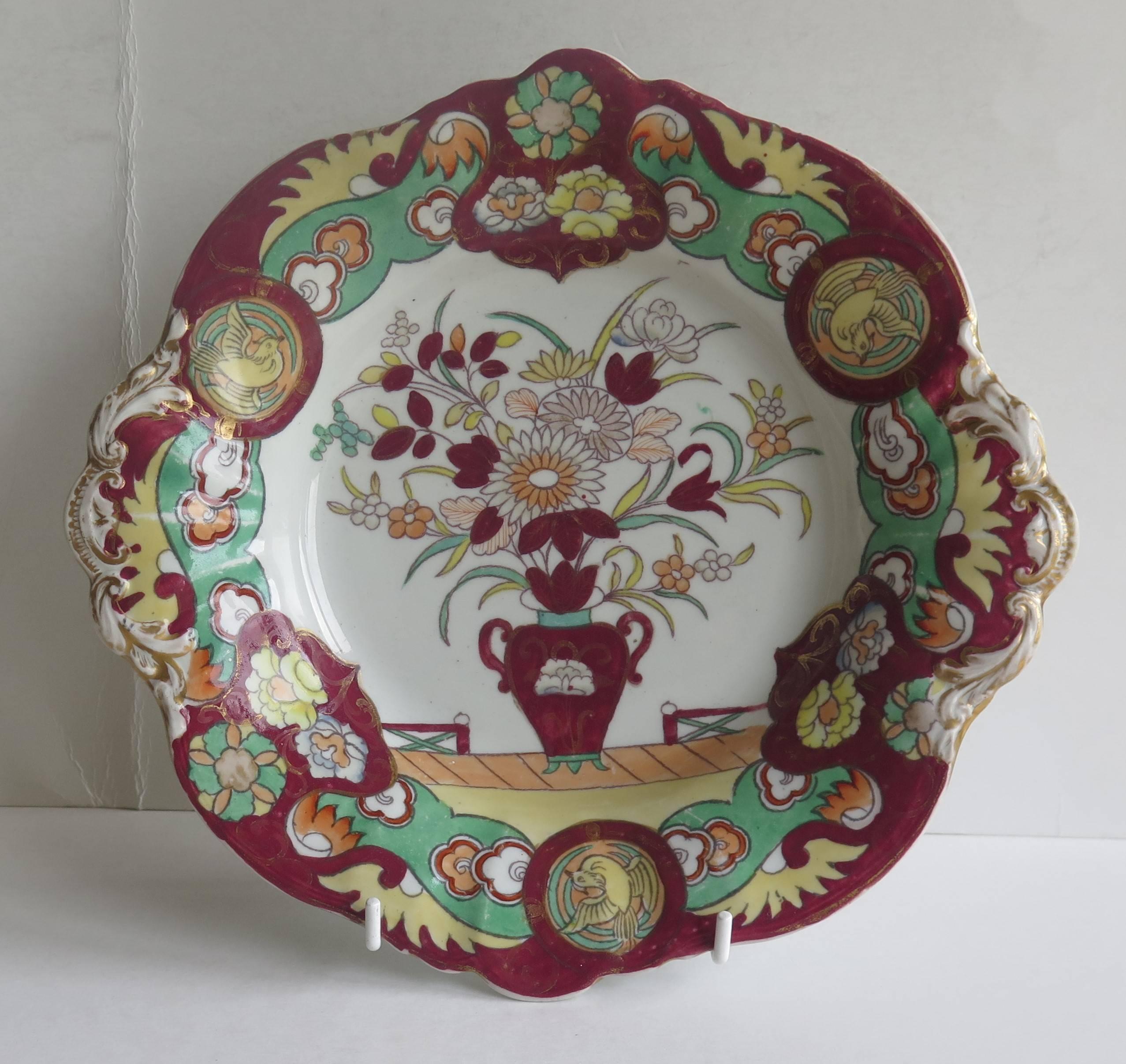 This is a very attractive two handled shallow Desert Bowl or Dish made by Mason's Ironstone Pottery, in the early 19th century.

The bowl is decorated in the Fence Vase and Dove chinoiserie influenced pattern, which shows a central flower filled