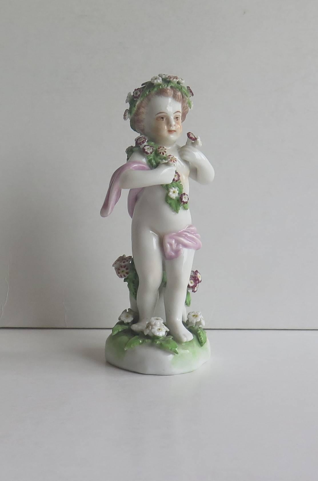 This is a very attractive porcelain figurine of a putti or cherub.

The figurine is good quality with sharply moulded, crisp decoration with garlands and grouped bunches of flowers. It is hand decorated in over-glaze enamels with flower and leaf