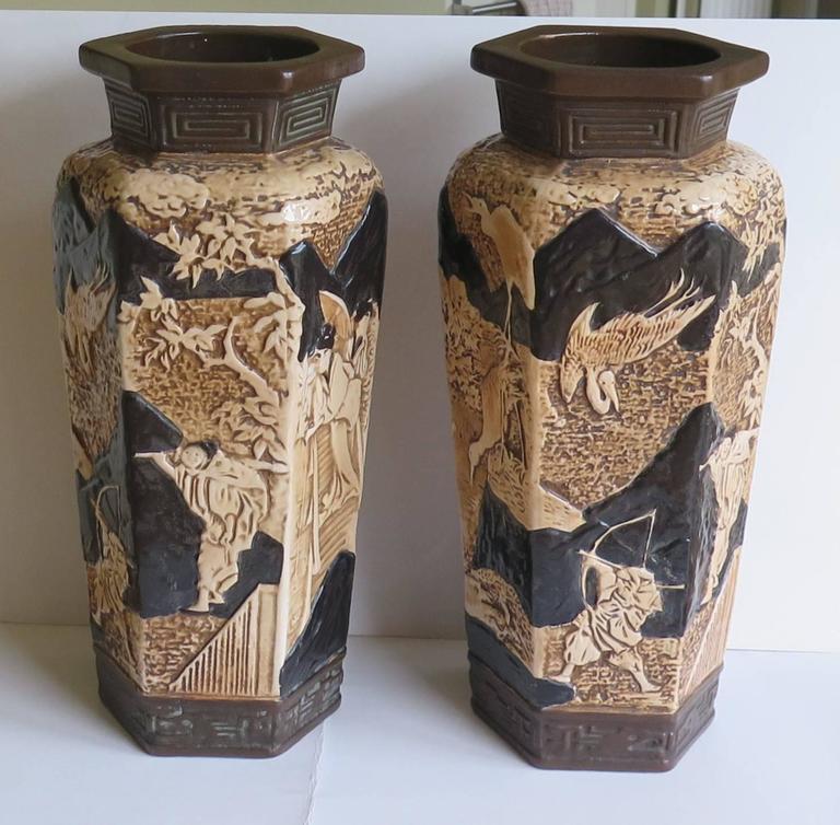 These are a very decorative and unusual PAIR of Large Earthenware Vases with oriental figure scenes, made by Bretby Ceramics, England, Circa 1914. 

The vases are 15 inches tall and are hexagonal in profile, featuring scenes of crane birds, and