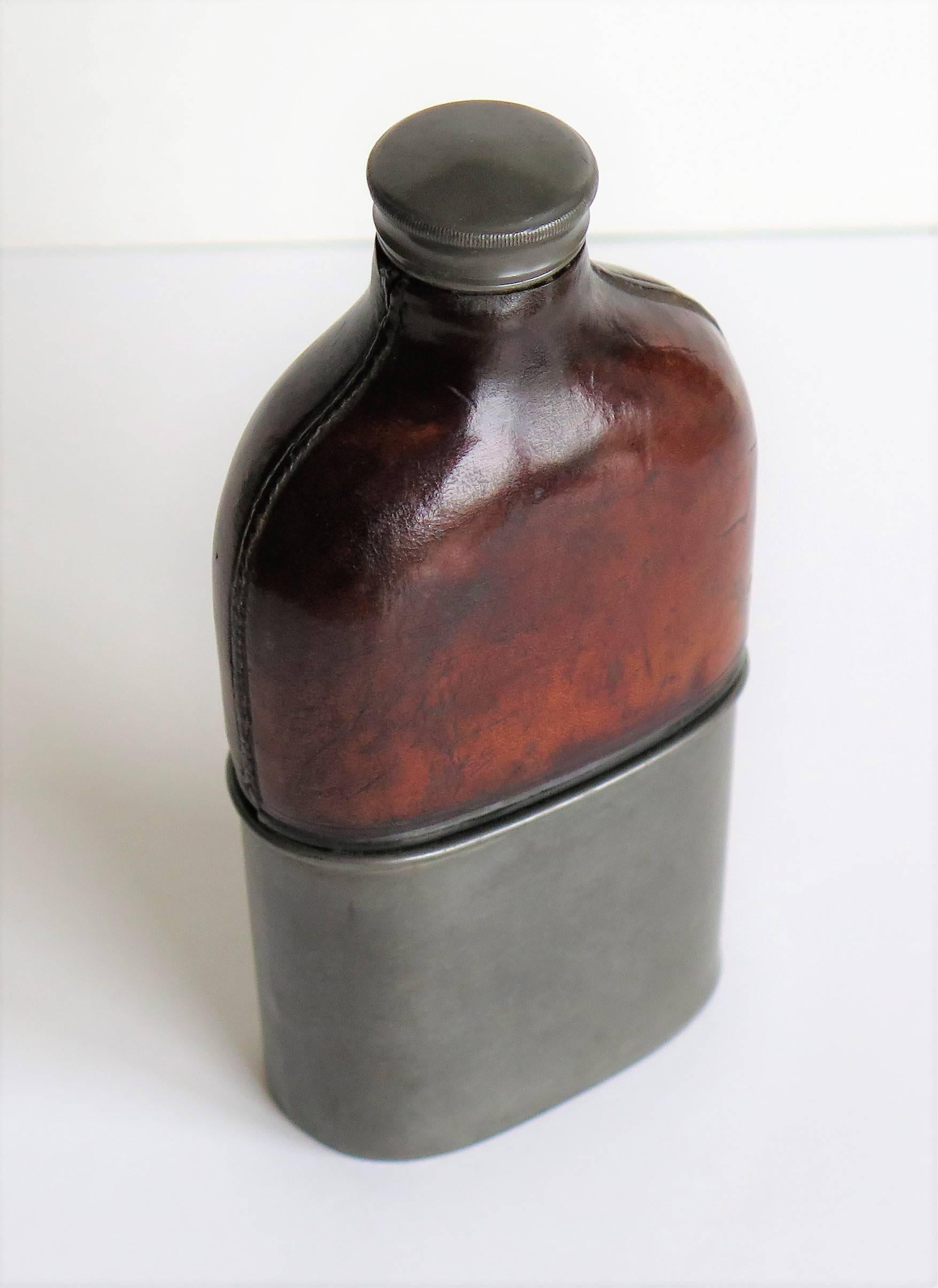 This is an antique hip flask dating to the mid or late 19th century.

The flask is made of moulded glass which has a brown leather upper section and a pewter base, the base also acting as a cup which is a snug fit over the base of the glass. The