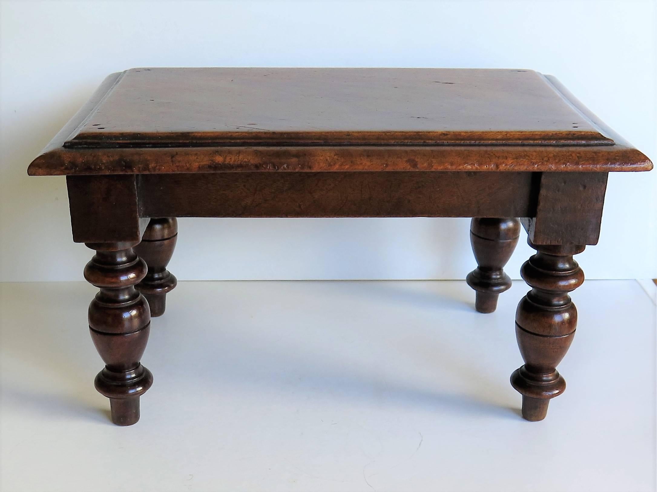 This is an unusual English low stand, candle stand or stool.

The top is rectangular, handmade from a single solid piece of mahogany or fruitwood, with a good molded edge. This top has developed a beautiful natural color and patina over many years