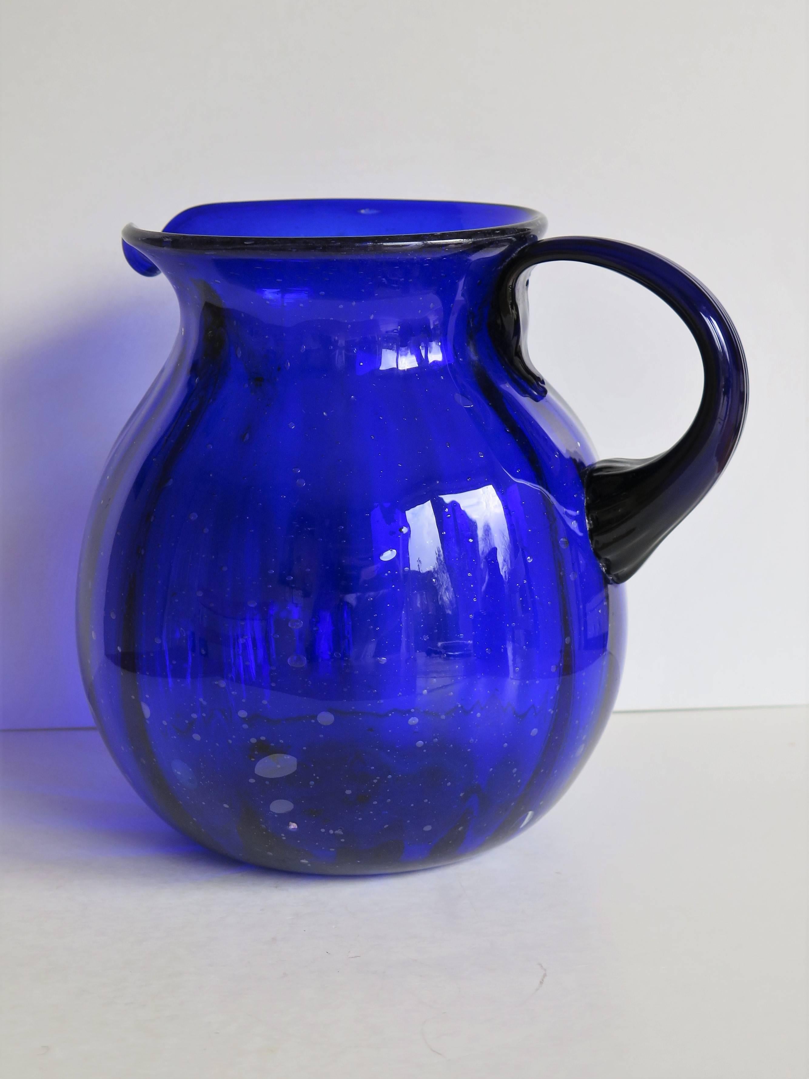 This is a very good hand blown large Jug or Pitcher in cobalt blue glass which we date to the earlier part of the 20th century, circa 1920s. 

This pitcher has a vertically fluted baluster shape with a good open top and pouring spout, with a loop