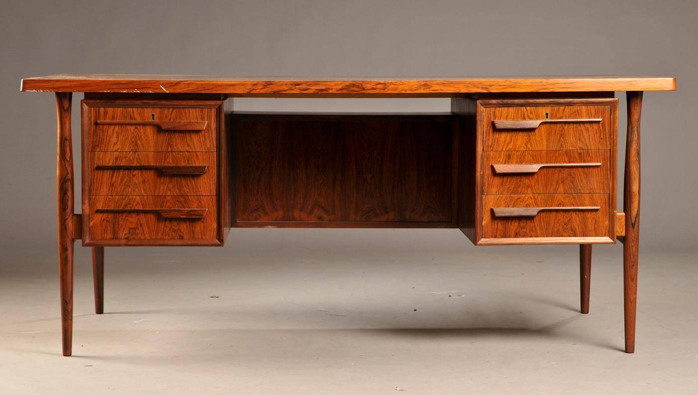 This desk made of rosewood in Denmark during the 1960s is attractive and functional. Typical of this period, the design is subtle and understated, allowing the fancy rosewood figure to dress up. 

The dark area on the tabletop will be the color of