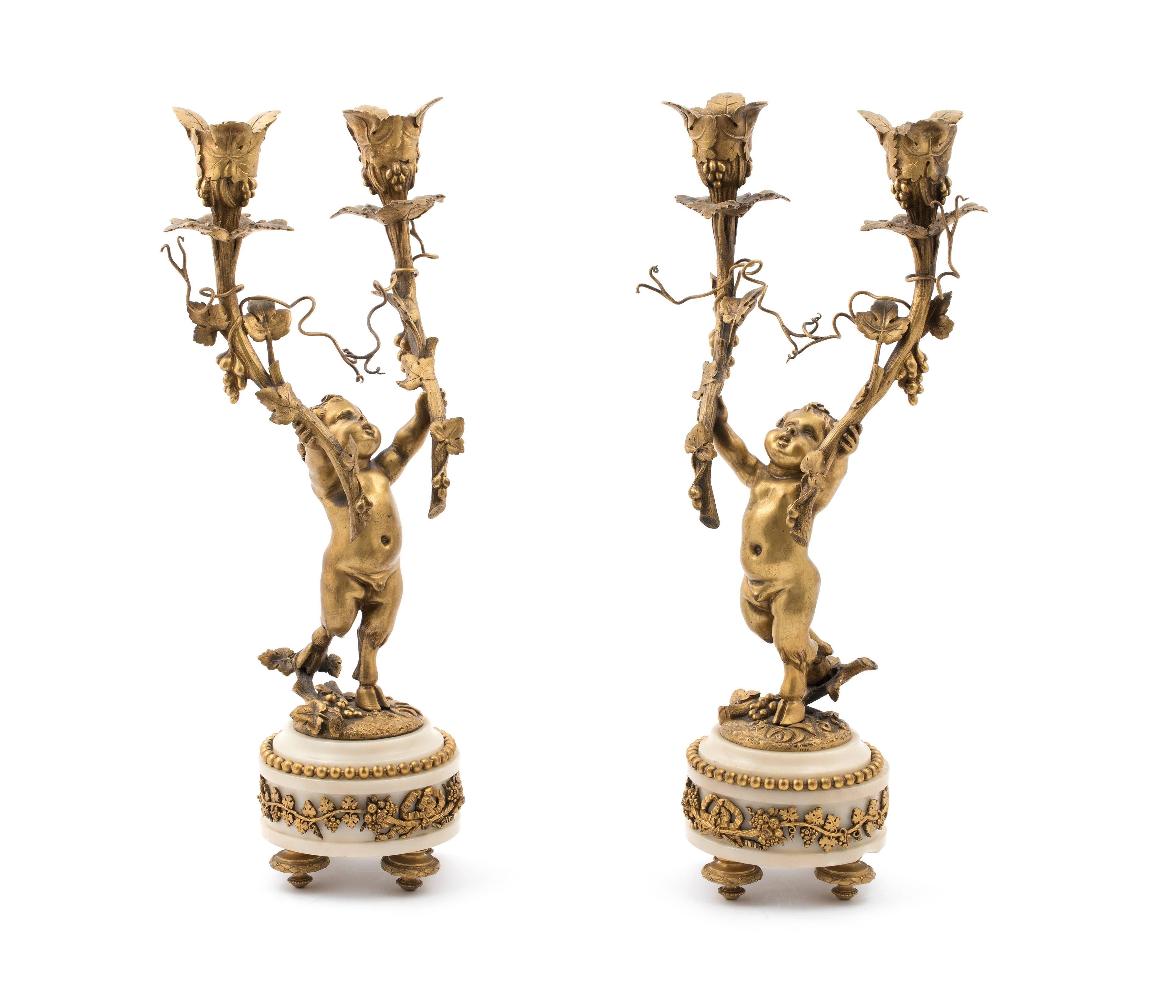 A pair of Napoleon III gilt bronze and marble two-light figural candelabra, in the manner of Jean-Michel Clodion, circa 1880.
In Louis XVI style, each modelled as a cherub holding aloft two grape vine shaped candle-arms with naturalistically