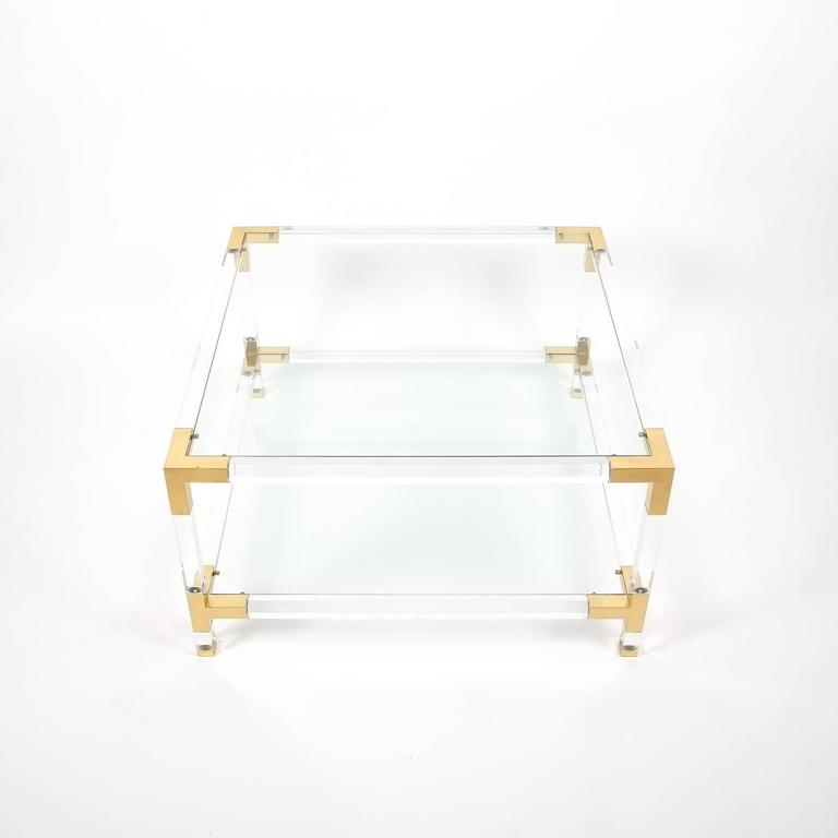Nicely sized 31x 31 inch French modernist two-tier Lucite coffee or cocktail table by Maison Jansen, Paris, 1970s featuring two clear glass top and lower glass shelves and polished brass corners. Very elegant piece in excellent condition. We ship