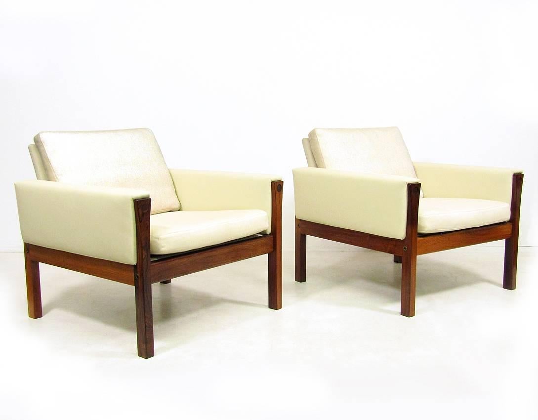 A pair of beautiful Danish 1960s "AP-62" lounge chairs by Hans Wegner for AP Stolen.
 
The solid rosewood frames, contoured legs and contrasting cream upholstery create a sense of mid-century luxury.
 
The arms have been re-upholstered