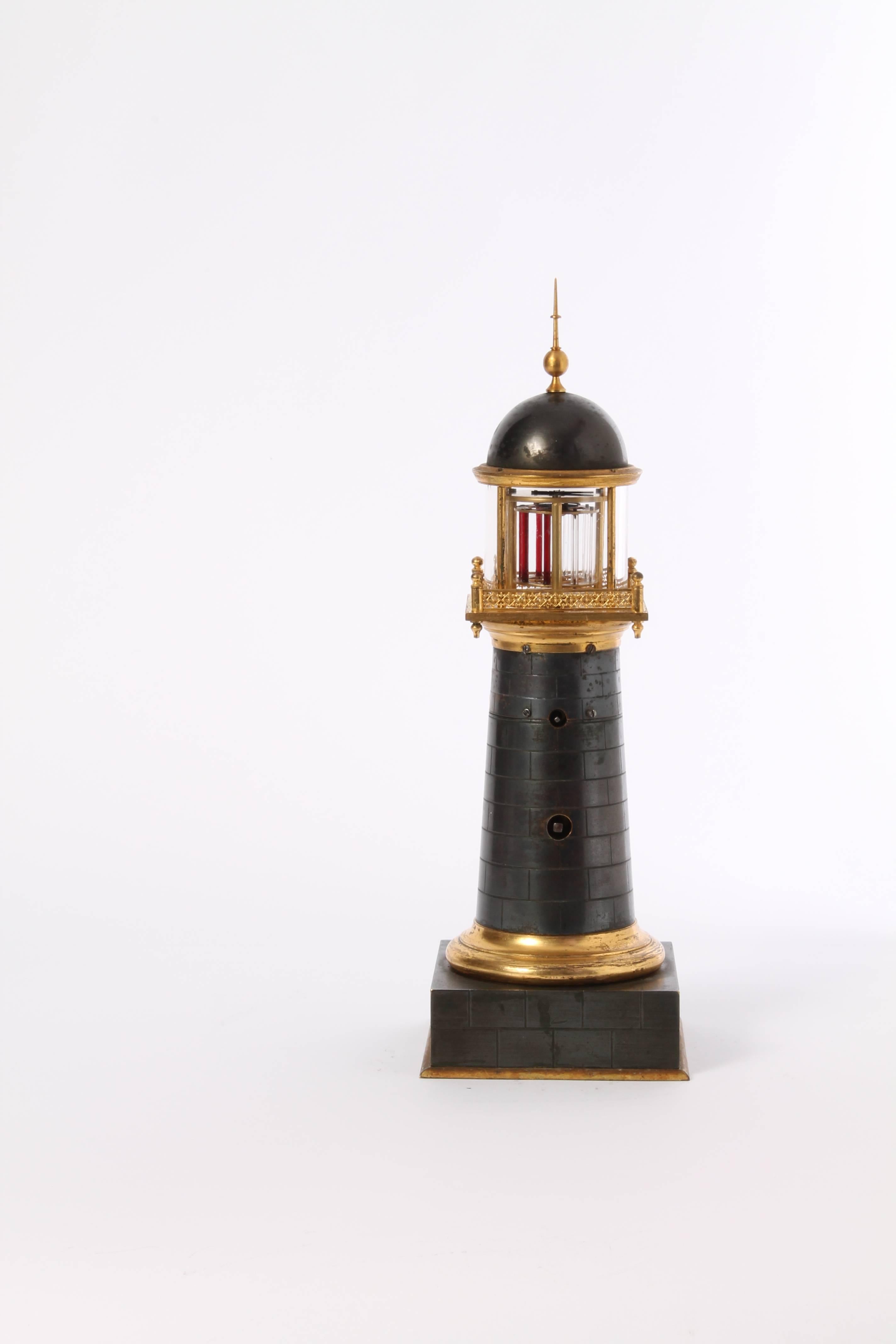 A small and amusing French bronze and gilt lighthouse timepiece with visible balance, circa 1850.

4-cm enamel dial with Roman numerals and blued hands fitted on a patinated brickwork lighthouse with gilt moldings, the upper part with pierced