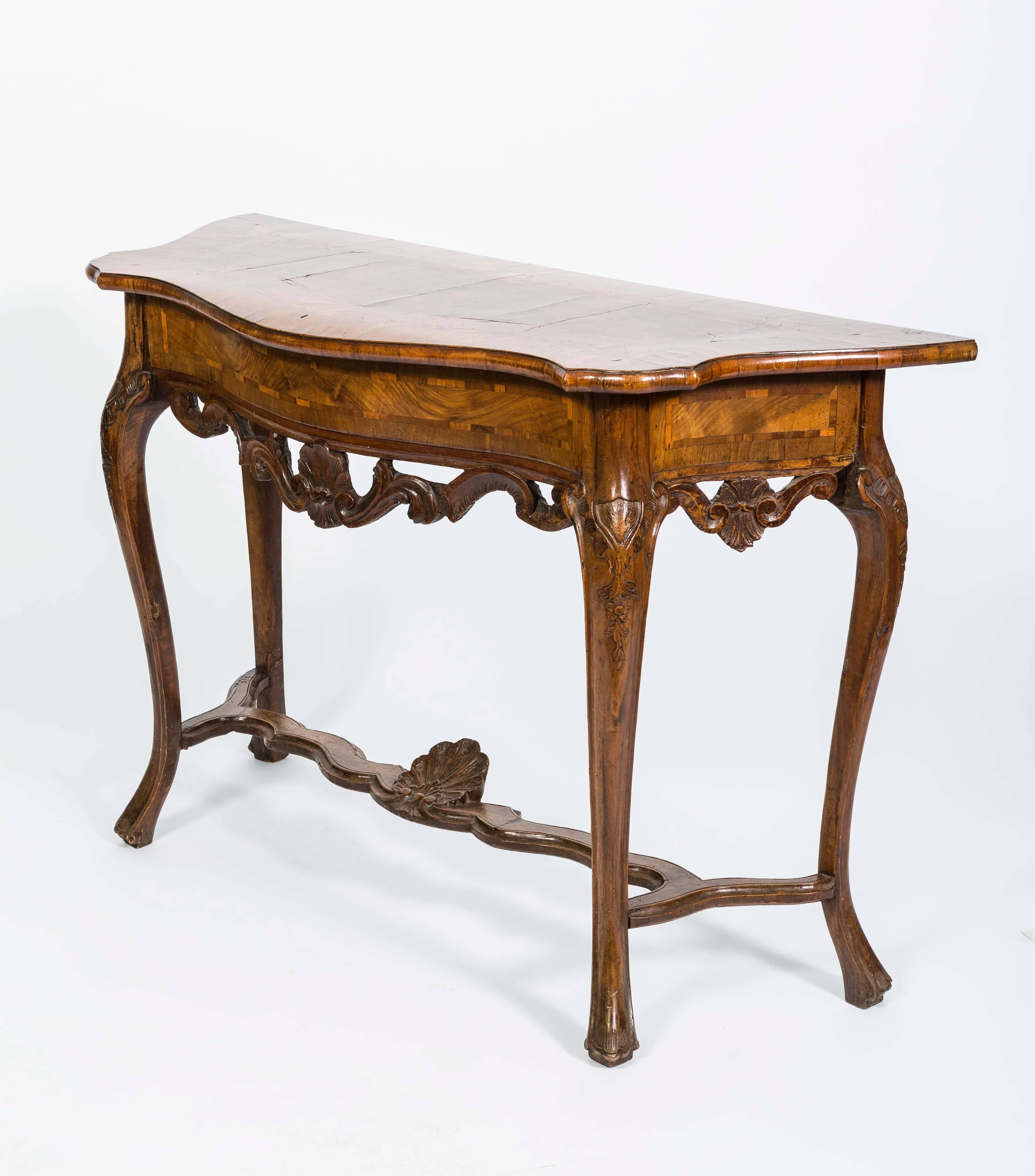 18th century Italian console table in walnut wood. The Italian console has four curved legs connected by a stretcher with a shell motif in the centre of the stretcher. The 18th century console table has a beautiful shaped top with a scroll design on