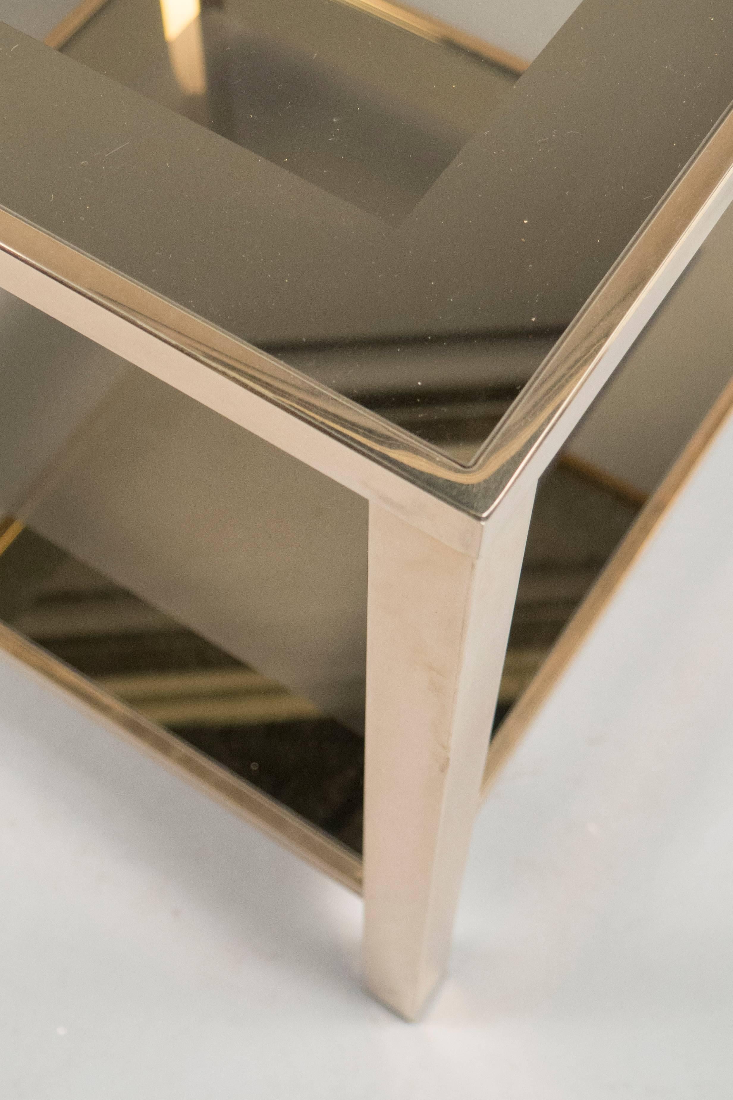 Square polished brass side tables featuring two smoked glass tops each.
 