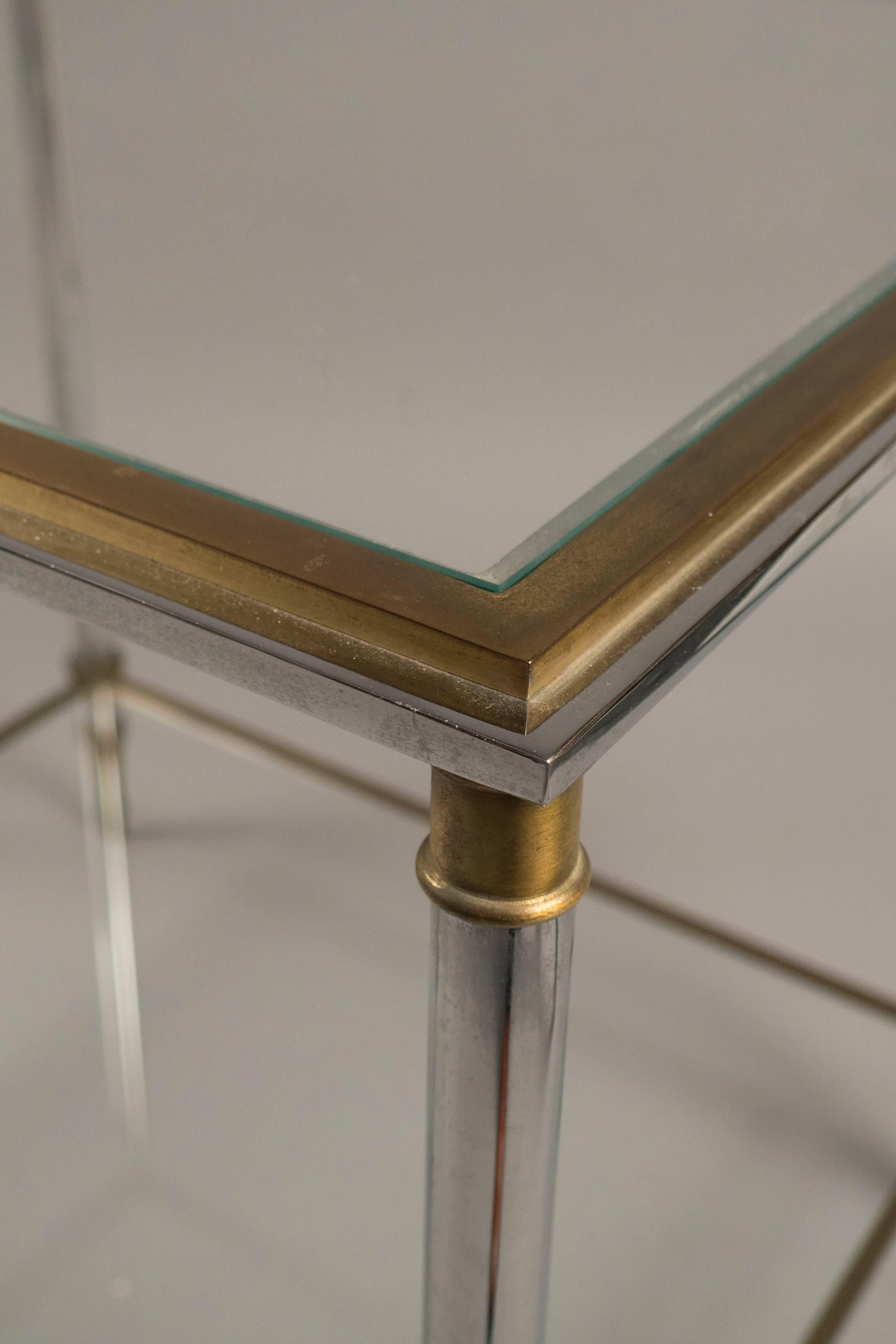 Polished steel and brass side tables, each featuring two tiers fitted with clear glasses.
  
