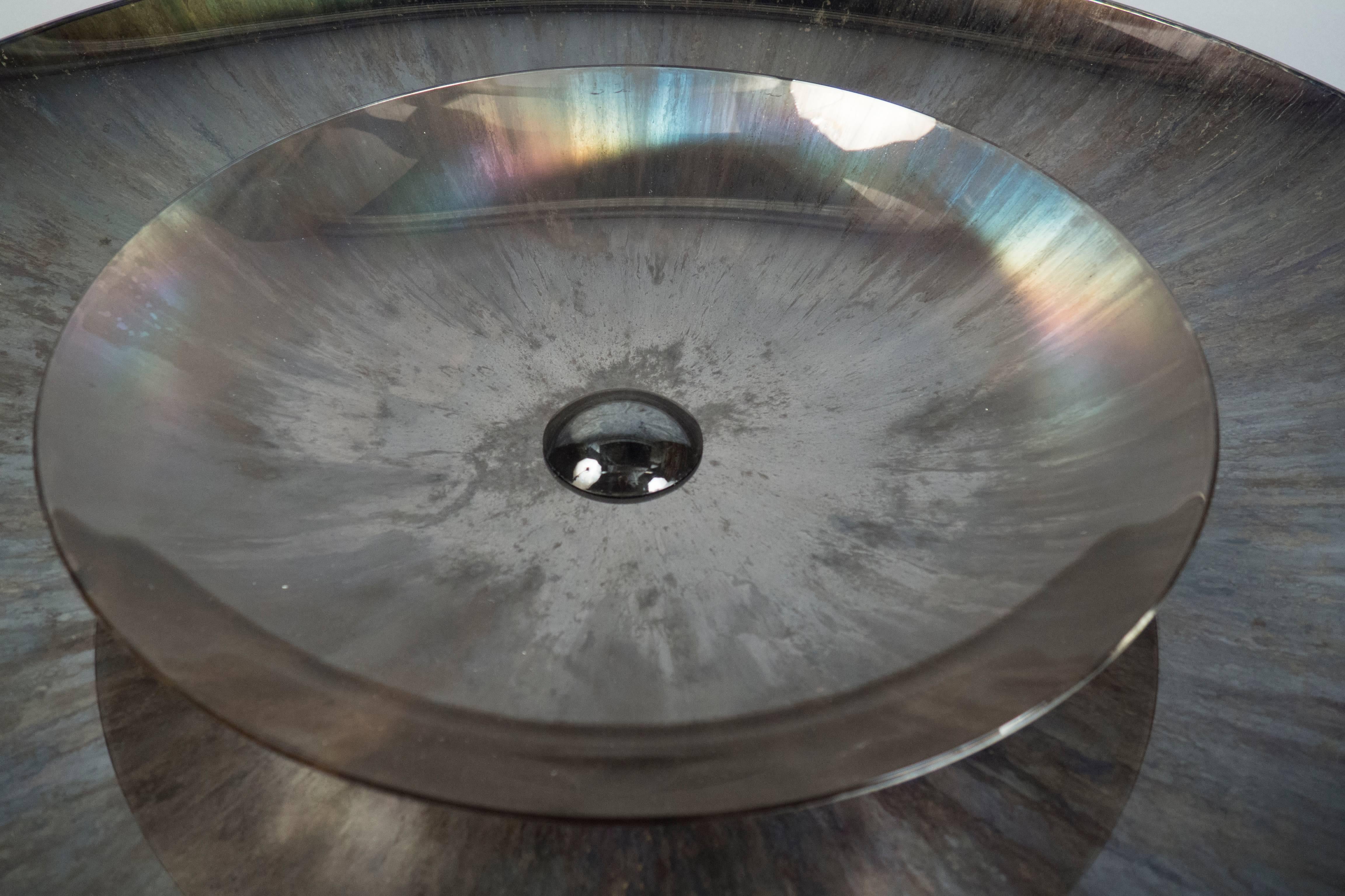 Slightly concave mirror plate with a second concave plate in the center, composed of a gray contrasting base color glass with some iridescence added to create a diffuse-pattern patina.